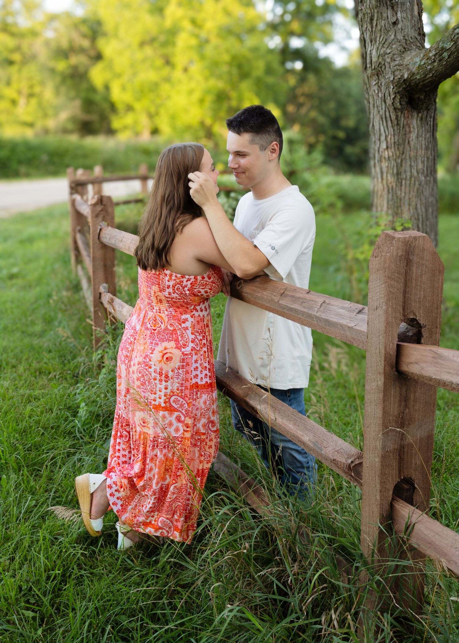 Young couple sharing a romantic moment by a rustic wooden fence in a lush green park setting.