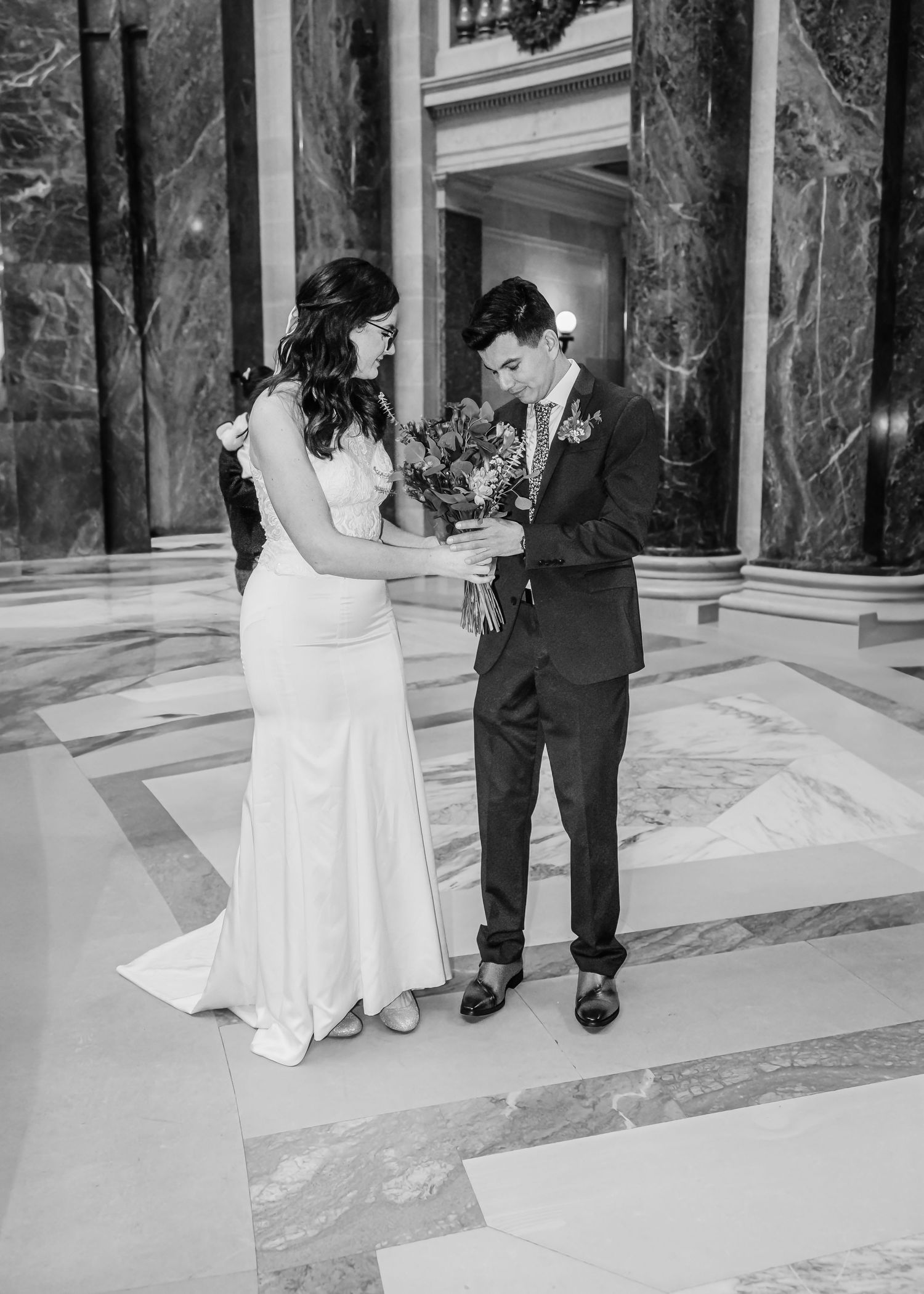 Black and white photo of bride and groom sharing a bouquet in an elegant marble wedding venue.