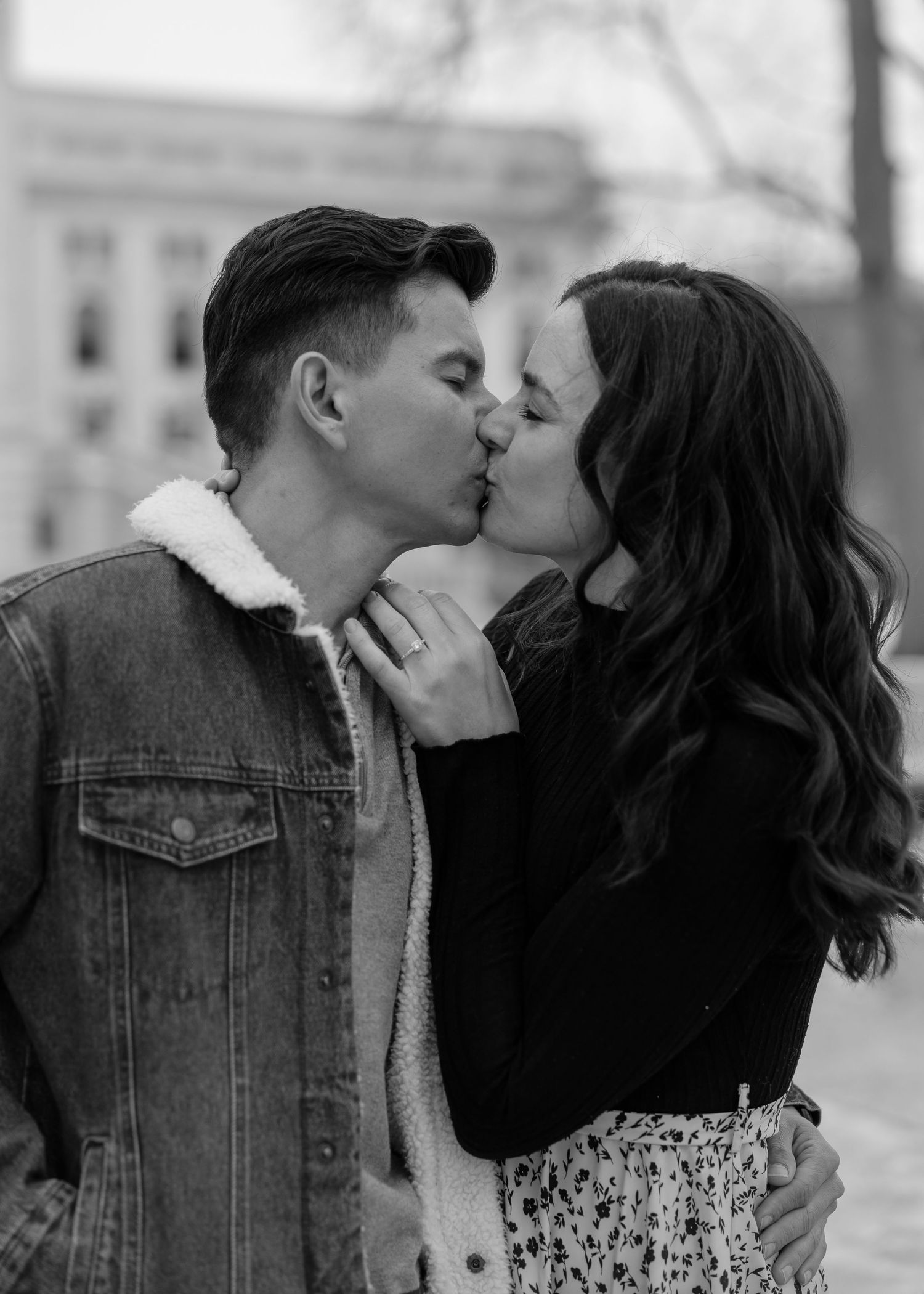 Black and white close-up of an engaged couple sharing a romantic kiss outdoors in winter.