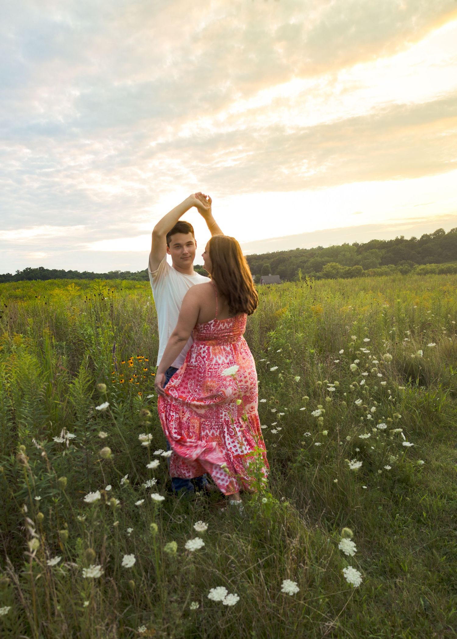 Couple dancing in a wildflower field at golden hour, woman in pink patterned maxi dress.