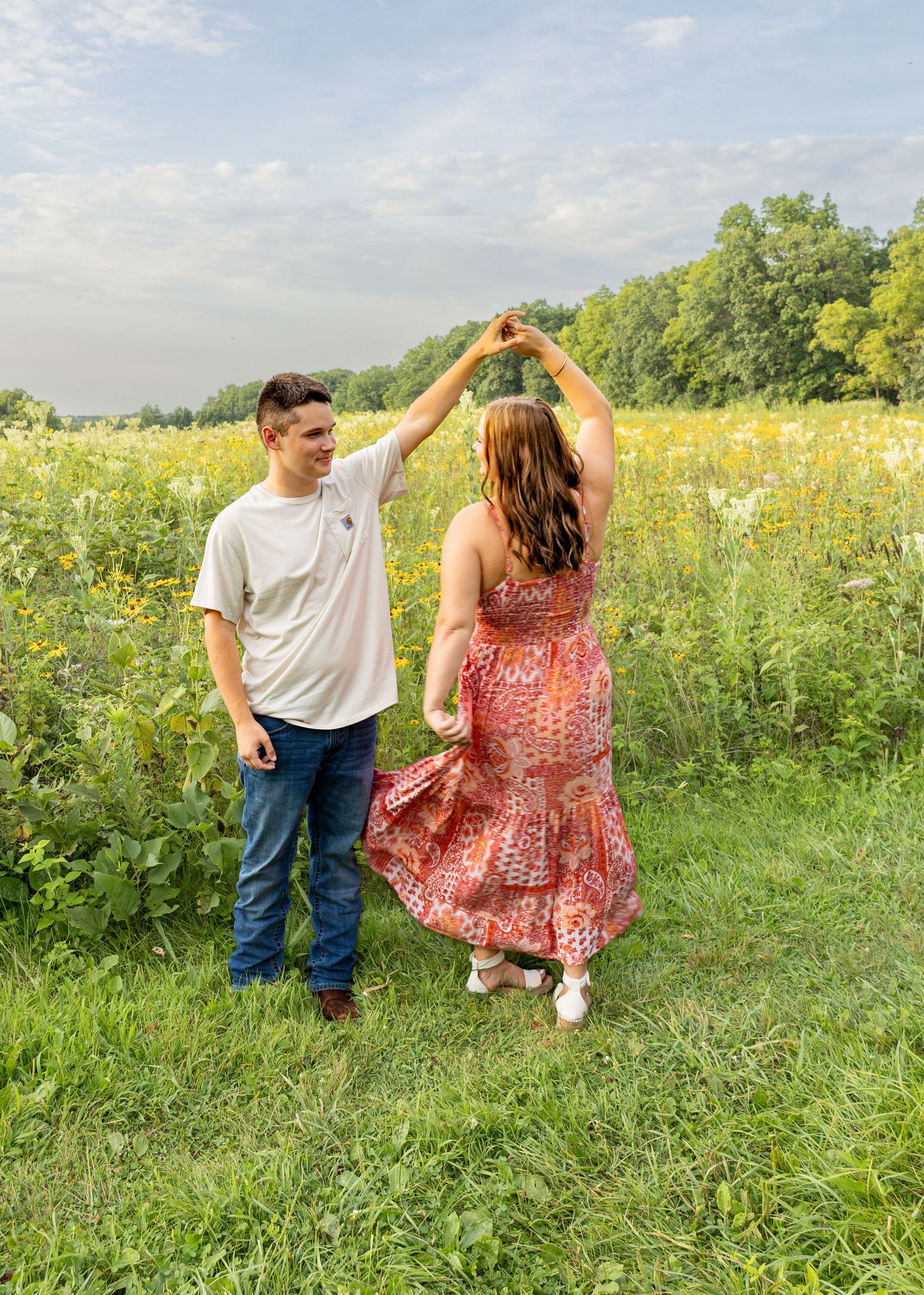 Young couple dancing outdoors in a sunny green meadow with wildflowers in background.