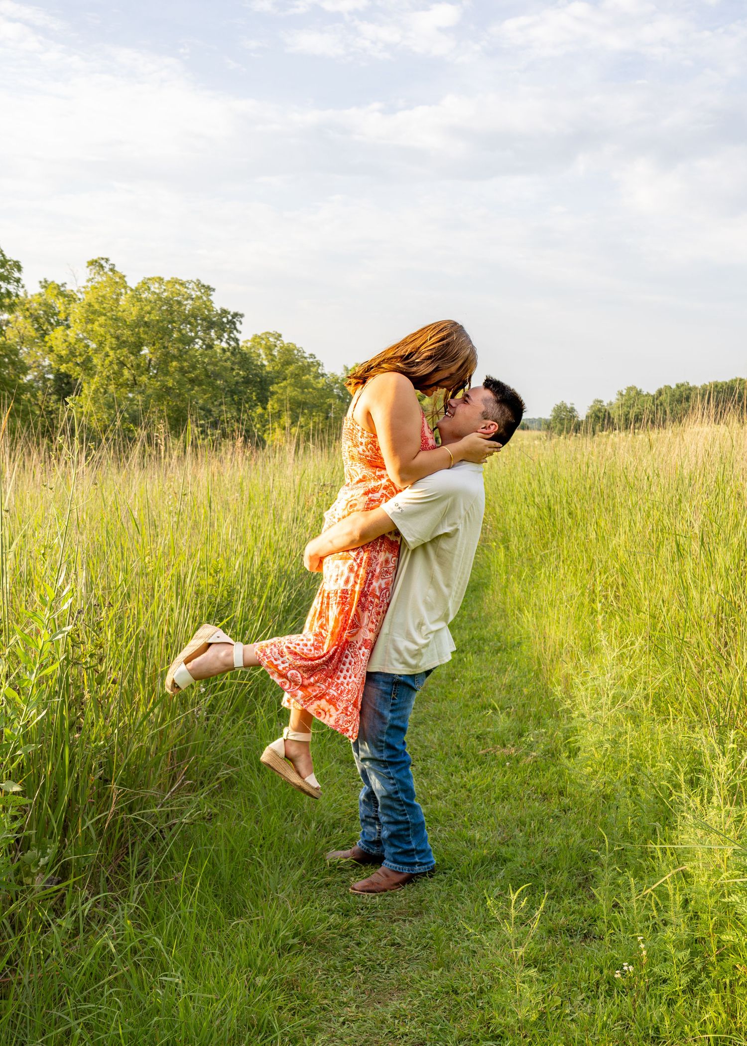 A man lifts and kisses his partner in a romantic moment along a sunny green meadow path.