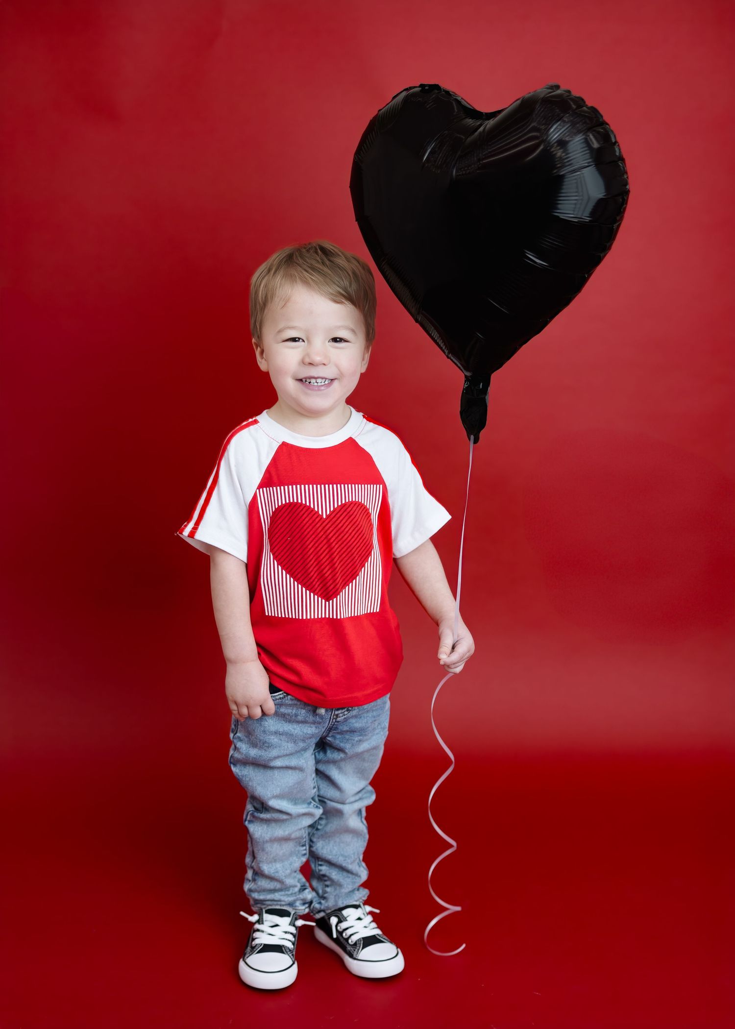 Smiling toddler holds black heart balloon in Valentine's Day photo session.