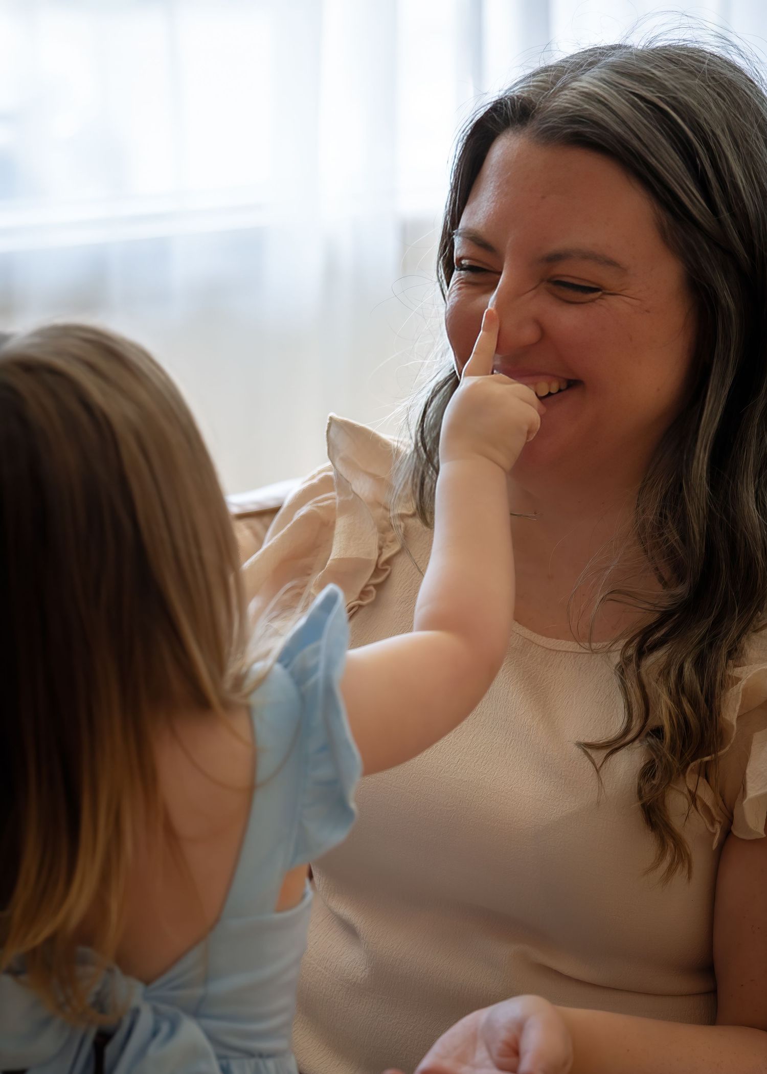 A woman laughs joyfully as a young child playfully touches her nose during a candid indoor moment.