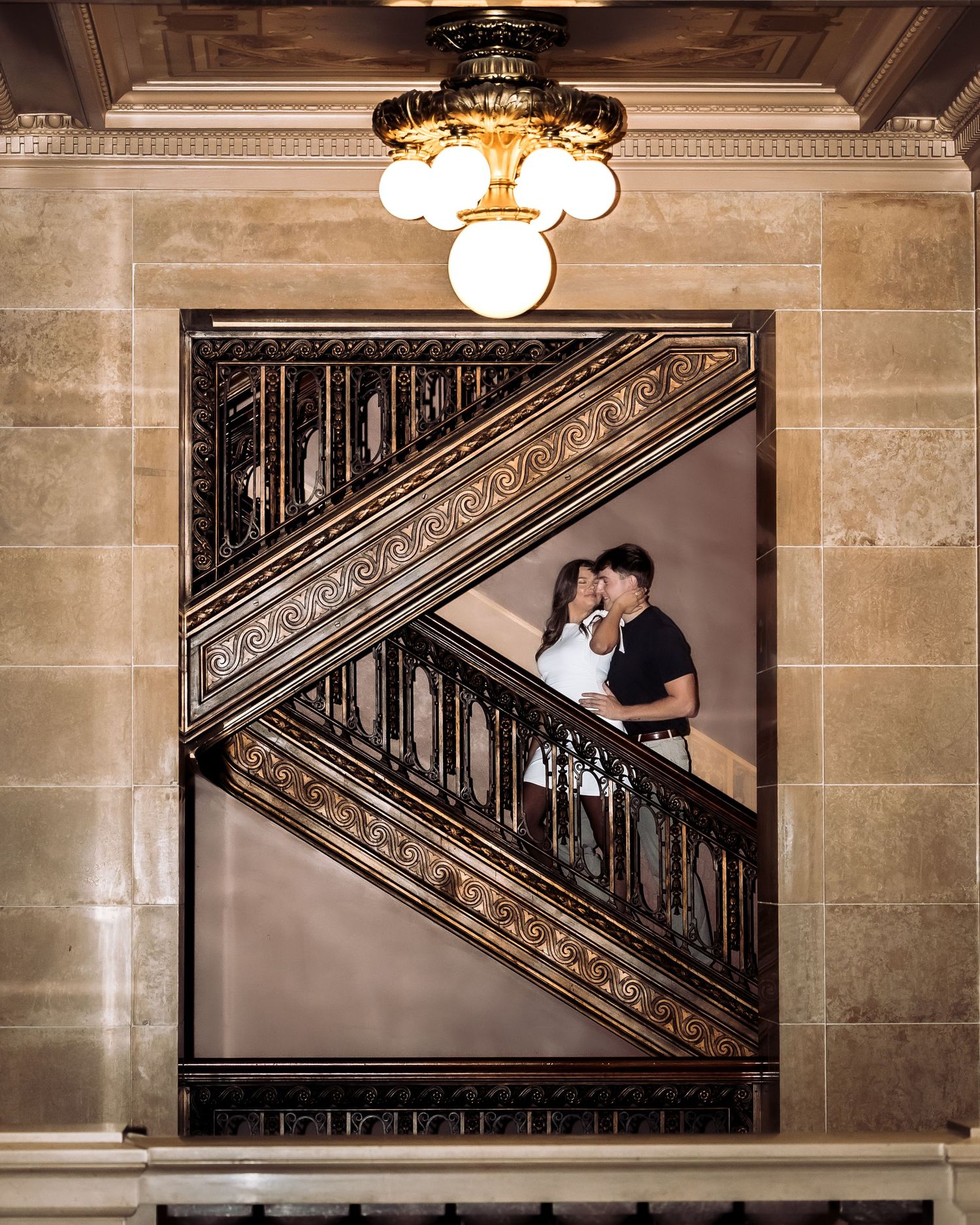 Couple sharing a romantic kiss on an ornate golden staircase inside a grand historic building.