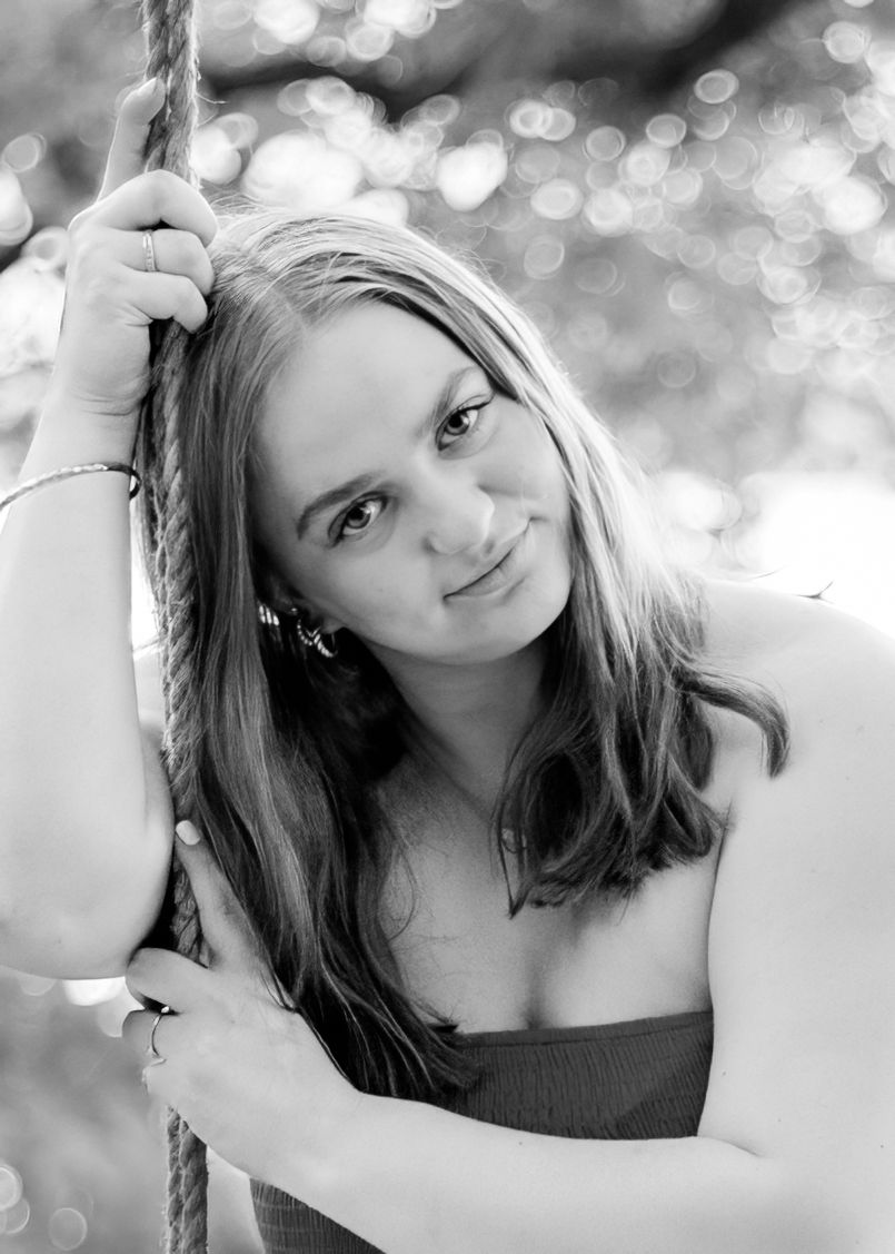 Black and white portrait of a young woman holding a rope swing with a soft bokeh background.