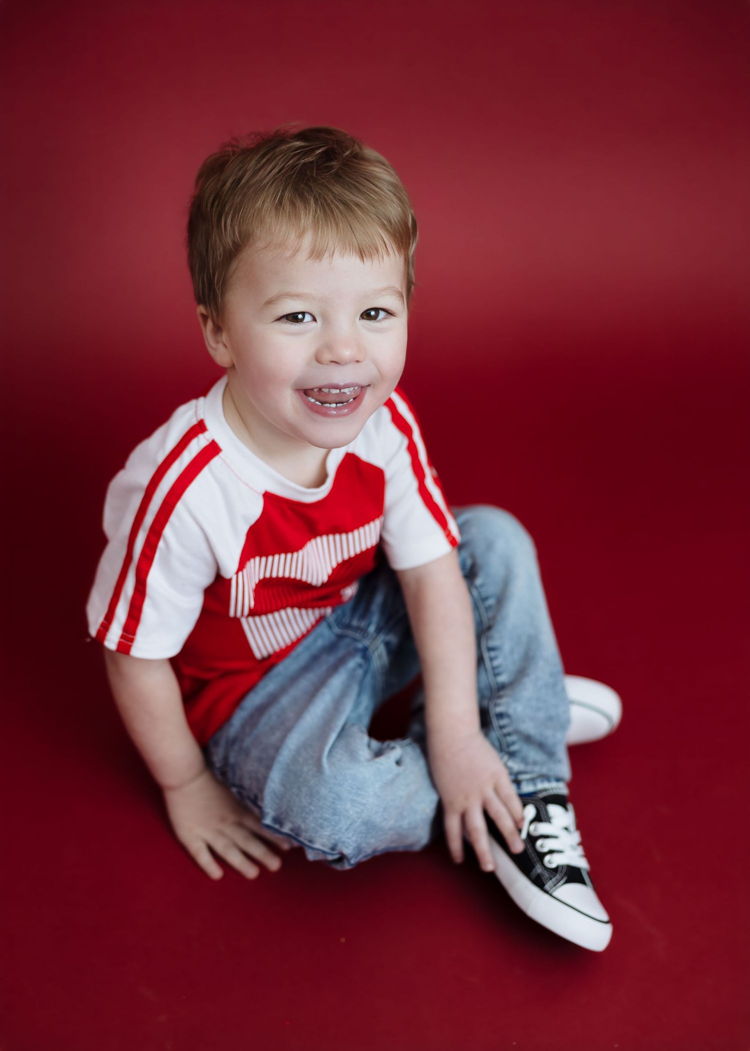 Happy toddler in red shirt sits laughing on red studio background.