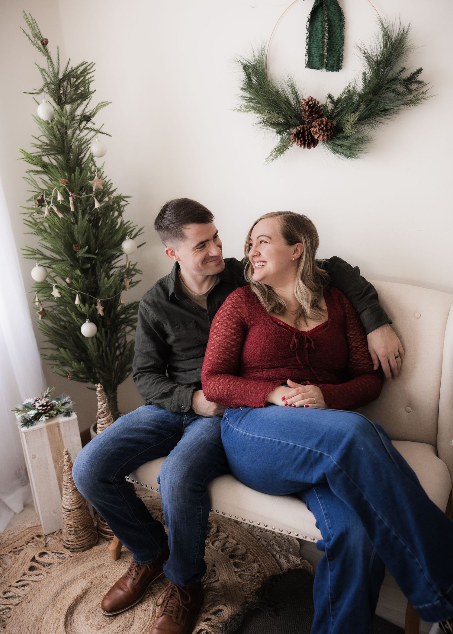 Couple sitting together on a sofa smiling at each other beside a Christmas tree.