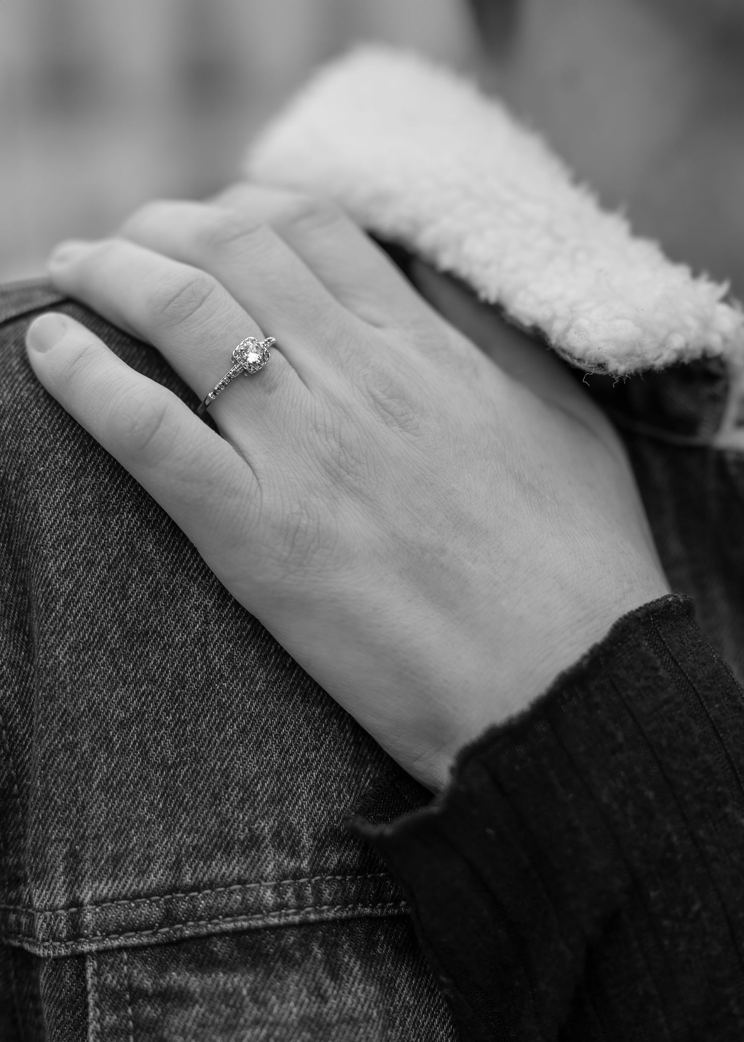 Black and white close-up of a woman's hand with a diamond engagement ring resting on a denim jacket.