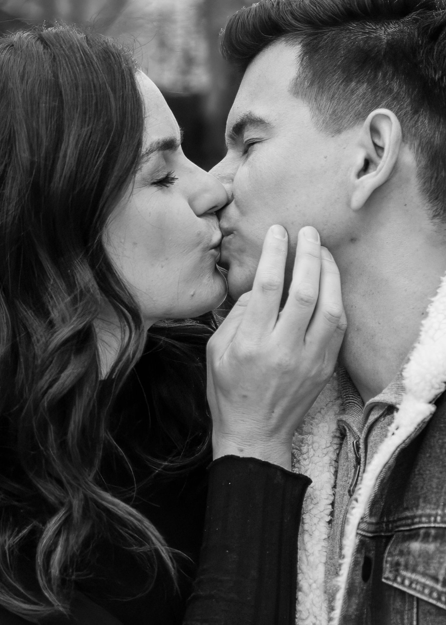 Black and white close-up of a couple sharing a romantic kiss outdoors.