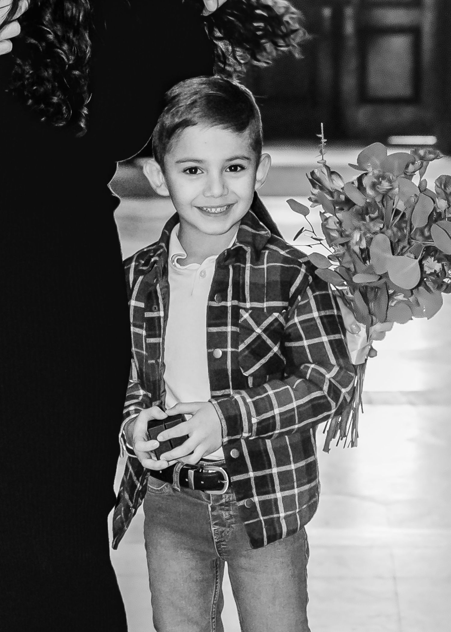 Smiling young boy in plaid shirt holding eucalyptus stems at a wedding ceremony, black and white photo.