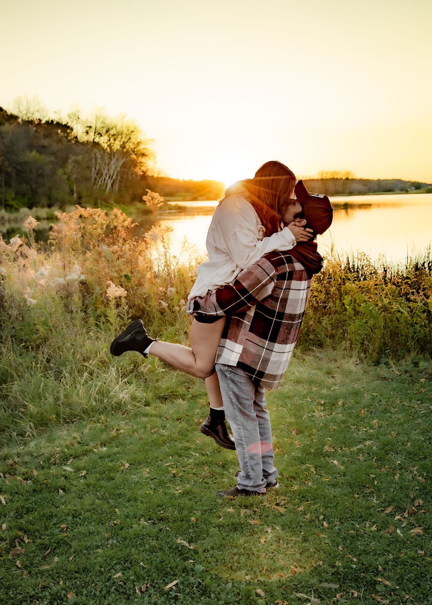 Man lifting woman in a joyful embrace by a lake during a glowing sunset.