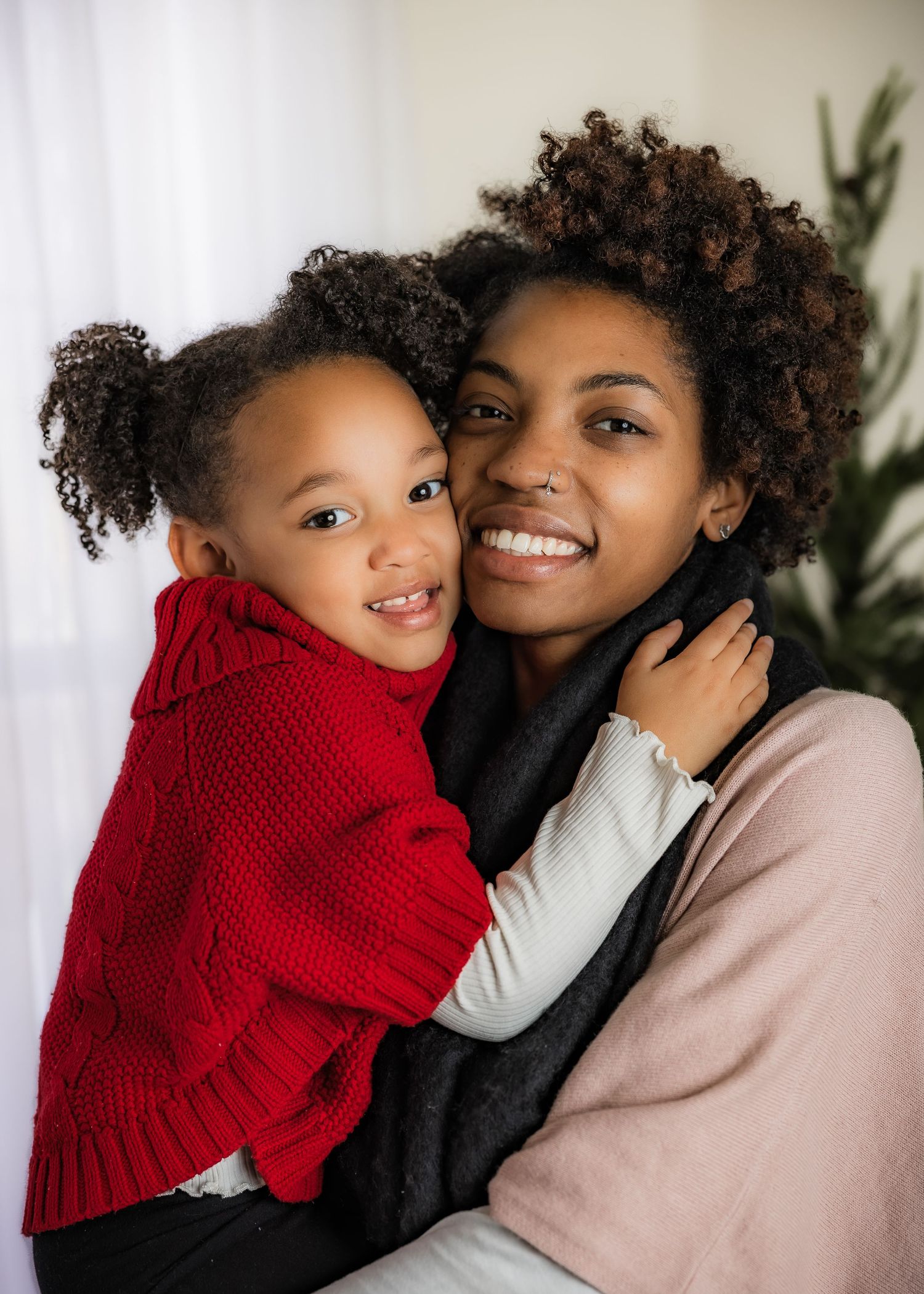 Smiling mother hugs young daughter in red sweater in a warm holiday portrait.