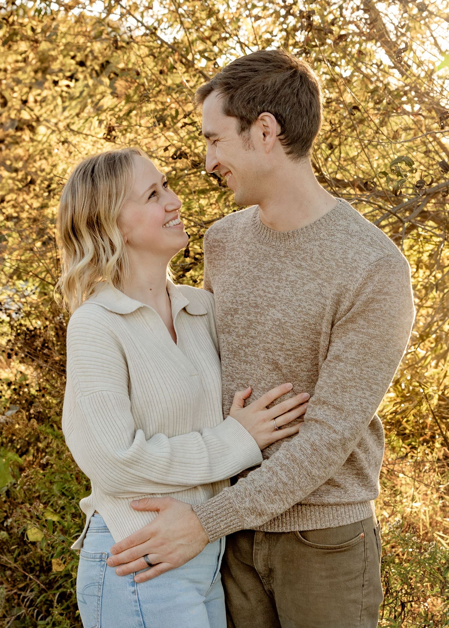 Smiling couple gazing at each other lovingly in front of golden autumn trees.