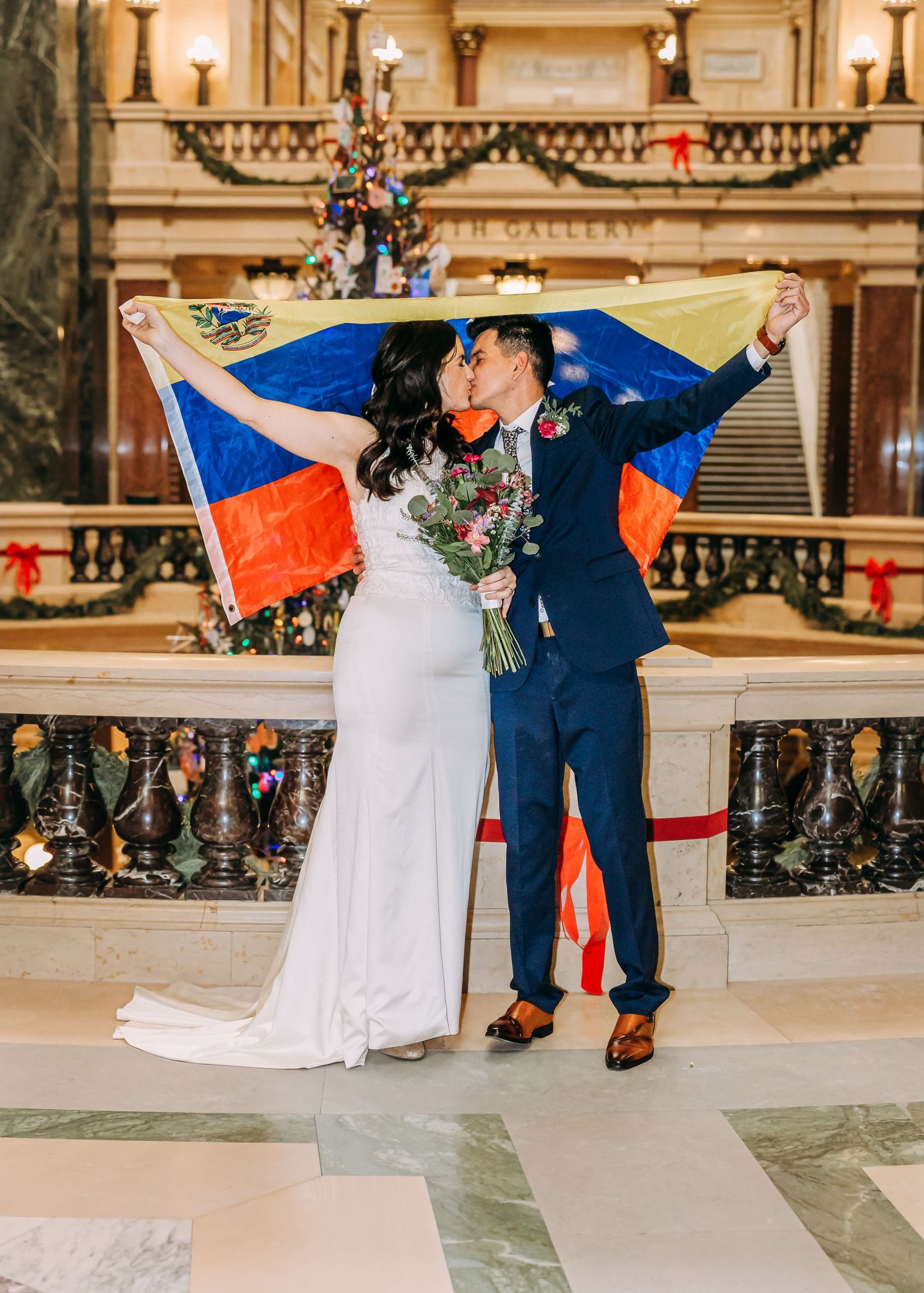 Couple kisses under Venezuelan flag in stunning capitol building wedding photo with holiday decor.
