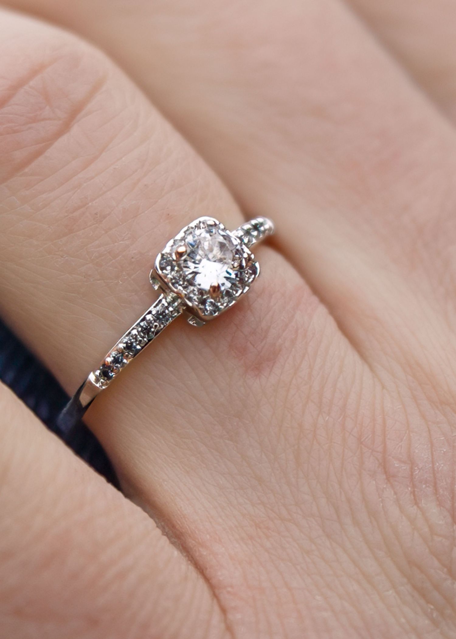 Close-up of a cushion halo diamond engagement ring in white gold on a woman's finger.