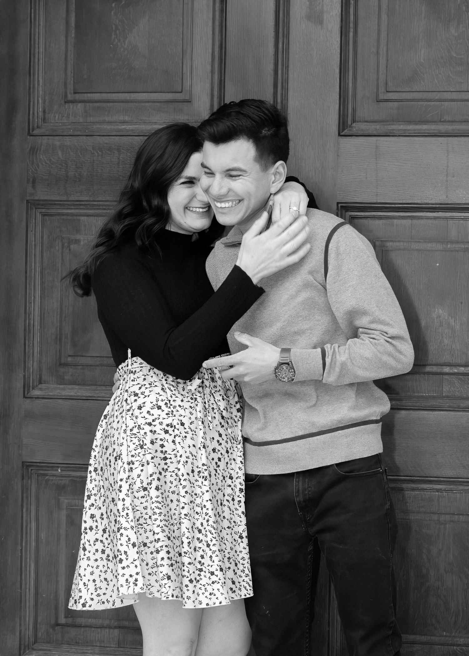 Black and white photo of a joyful couple embracing and laughing together in front of a wooden door.