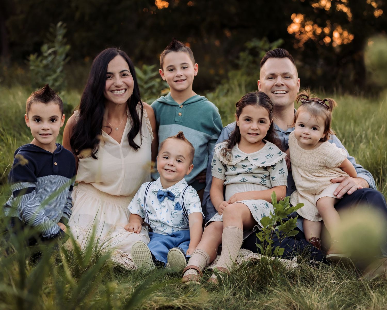 Happy family of seven smiling together outdoors in a grassy field at golden hour sunset.