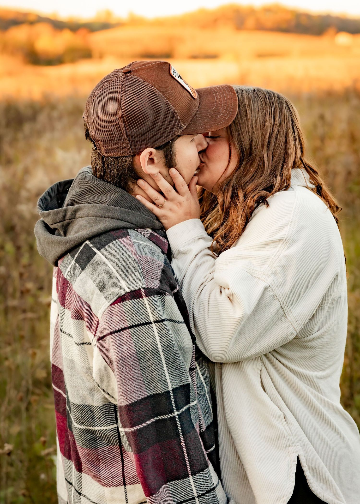 Couple sharing a kiss in open field during warm golden sunset light.