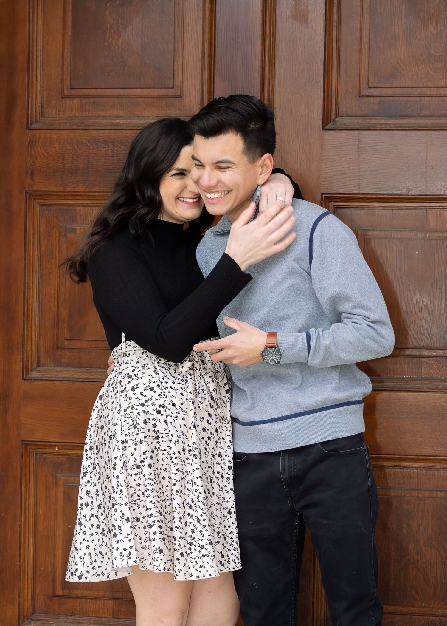 A laughing couple shares a joyful embrace leaning against large wooden doors at a historic building.