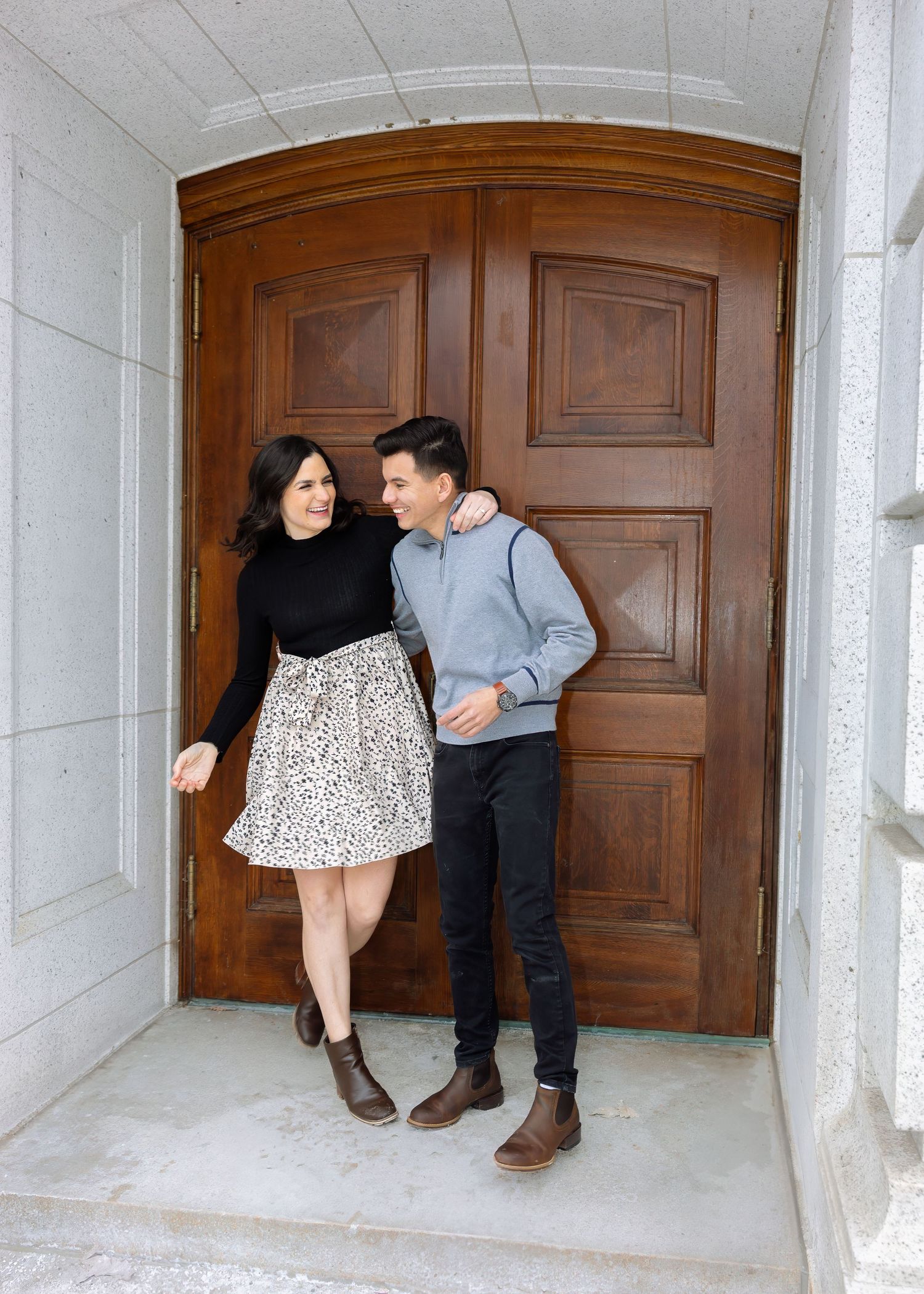 Happy couple walking and smiling at each other in front of elegant wooden double doors at a grand entrance.