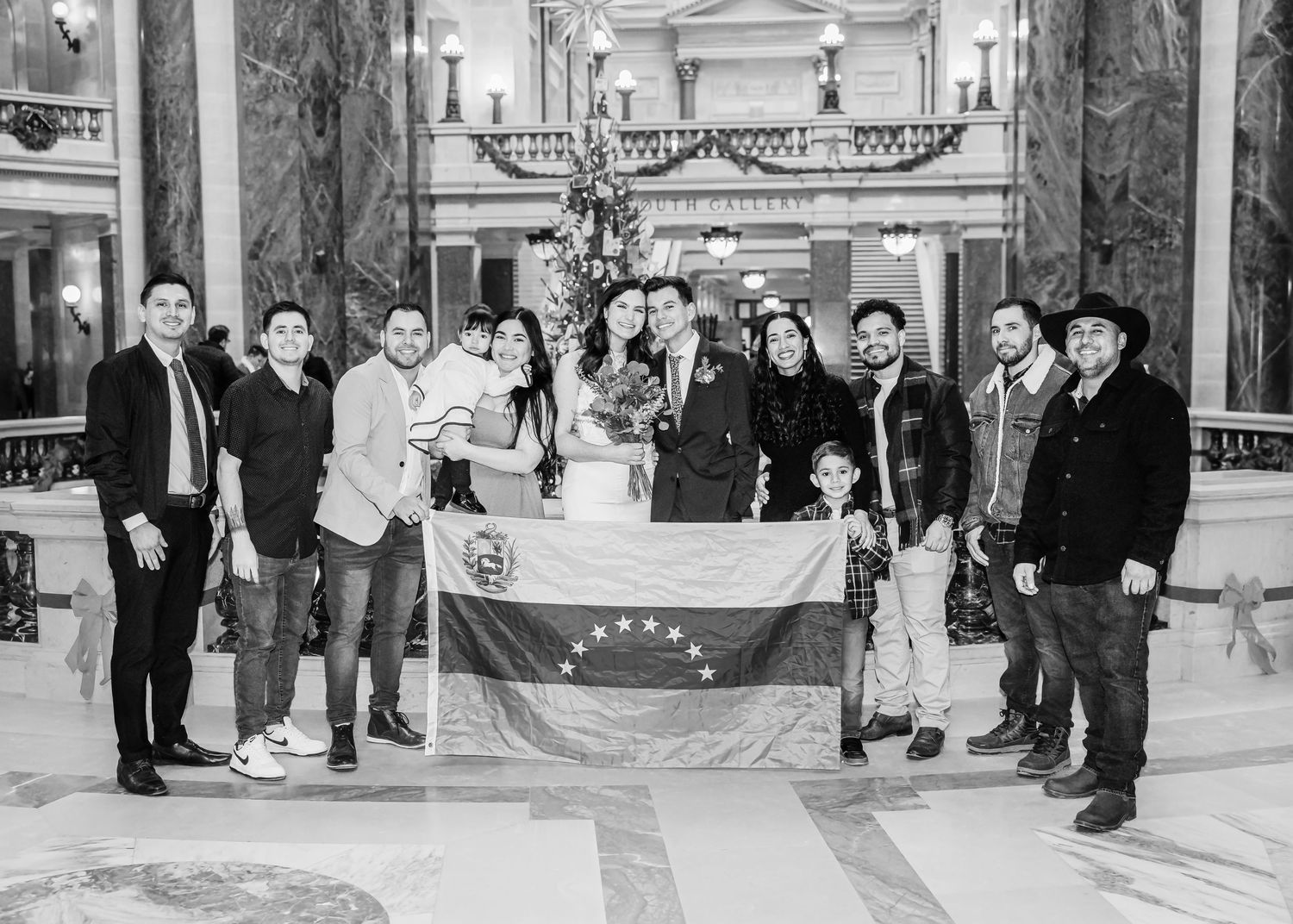Wedding group photo with family proudly displaying a Venezuelan flag in an ornate decorated hall.