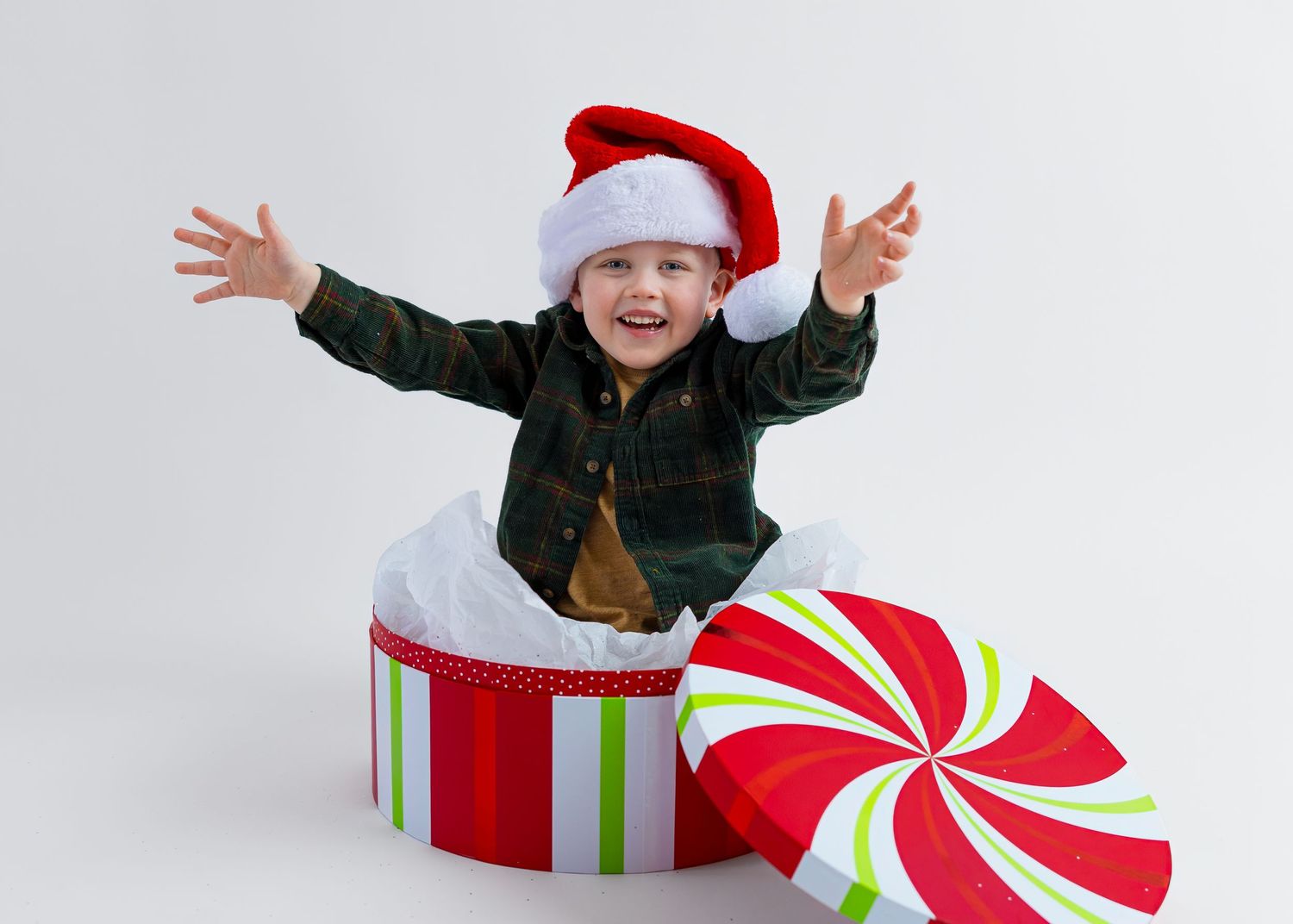 Excited child in Santa hat with arms outstretched popping out of large Christmas gift box.