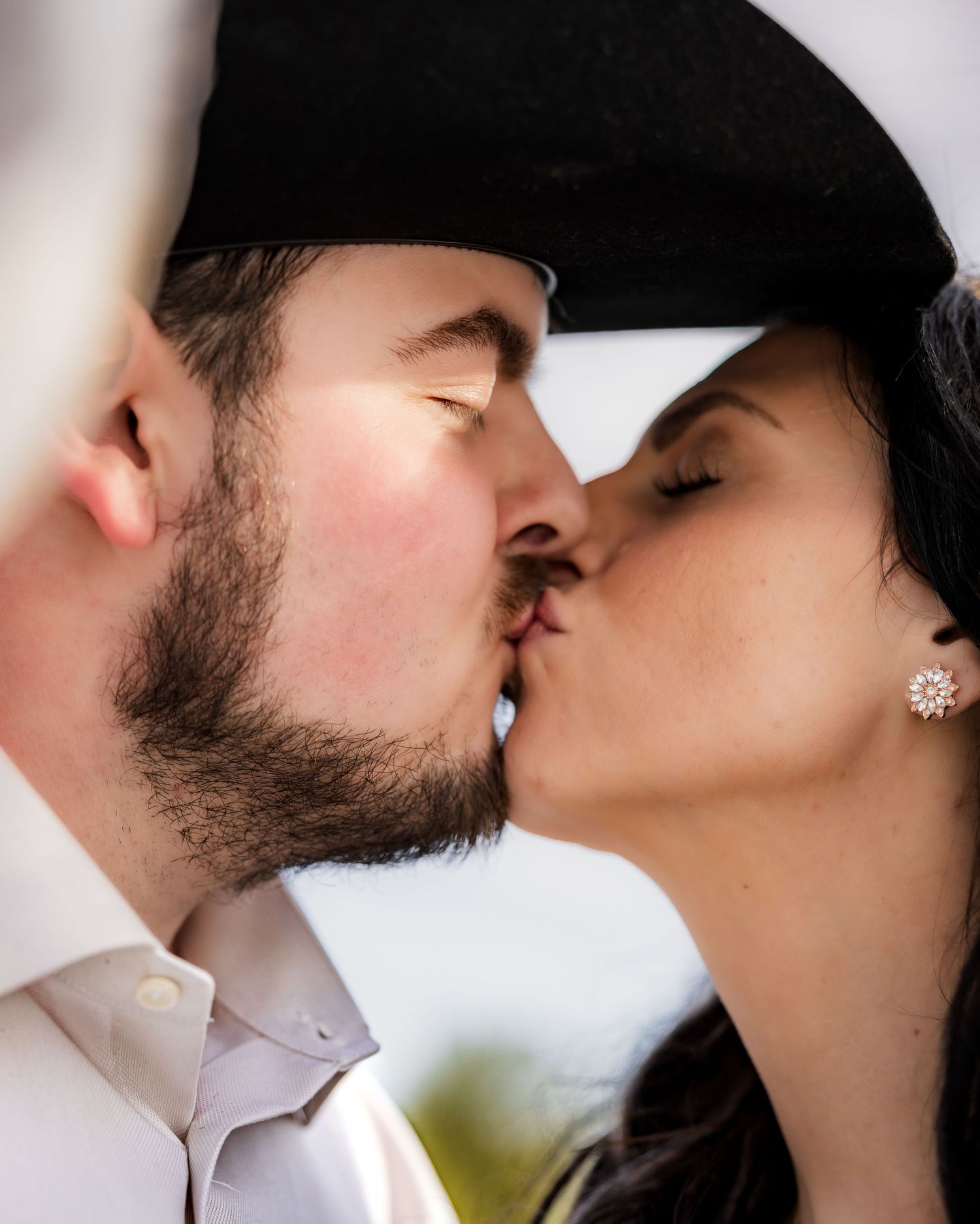 Couple sharing a romantic kiss, man wearing a black cowboy hat and white shirt, woman with diamond earrings.