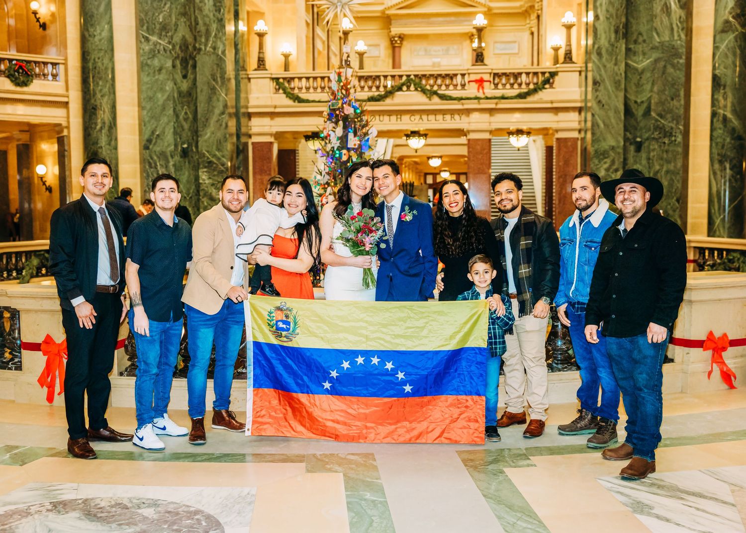 Wedding group photo with Venezuelan flag displayed proudly in decorated marble building.