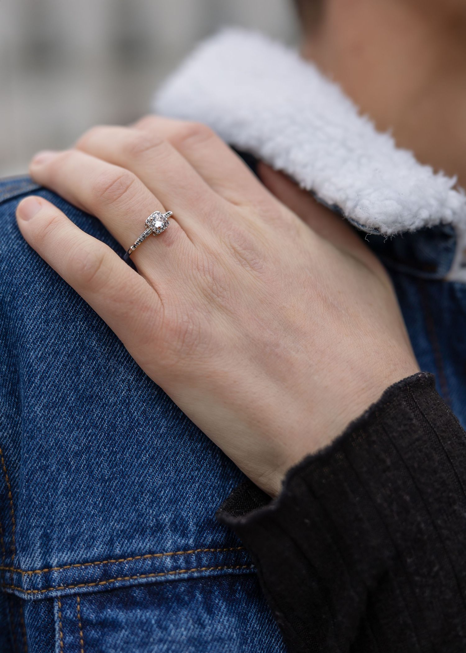 Close-up of a woman's hand displaying a diamond engagement ring resting on a man's denim jacket.