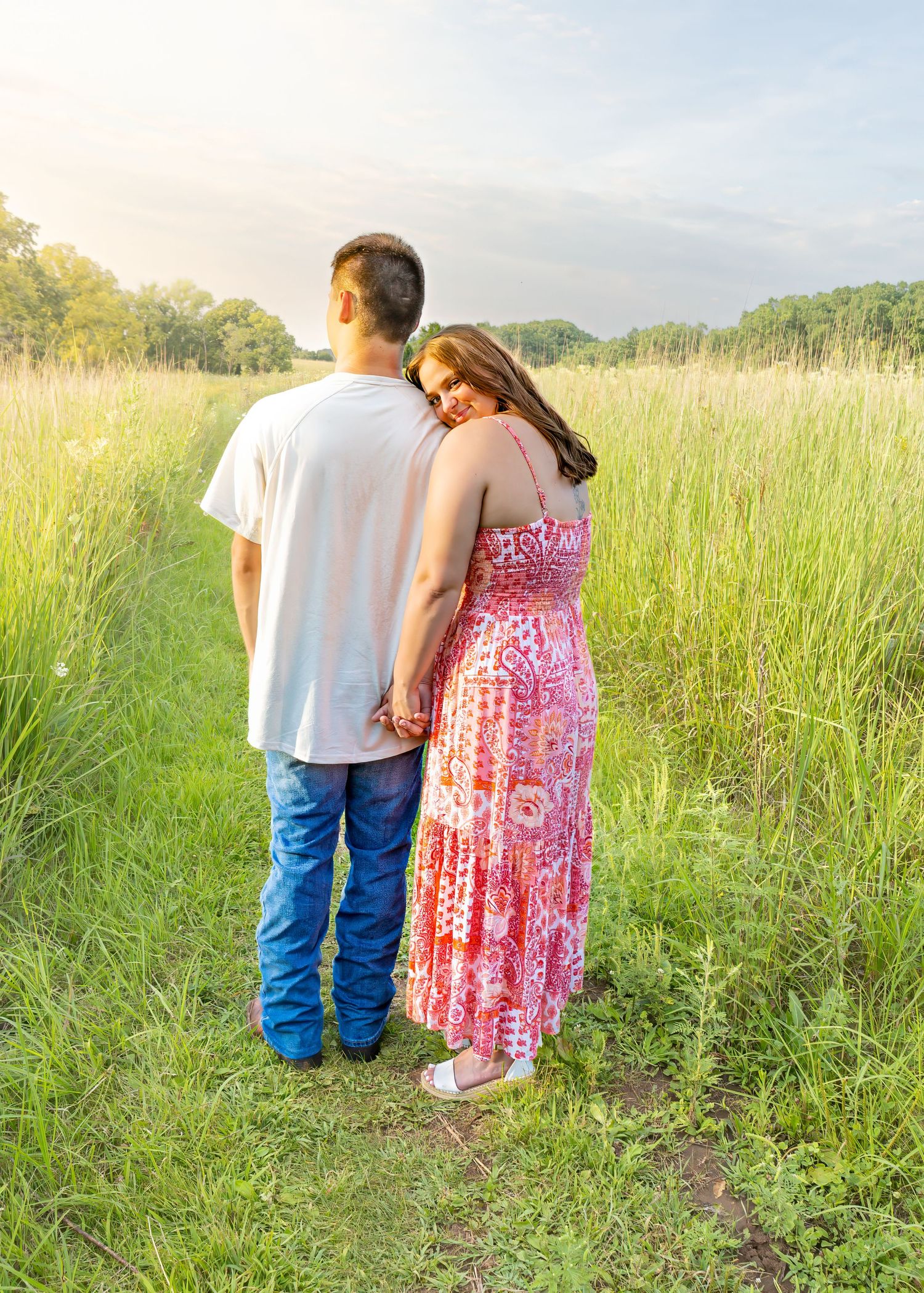 Couple holding hands gazing into a scenic green meadow under a bright summer sky.