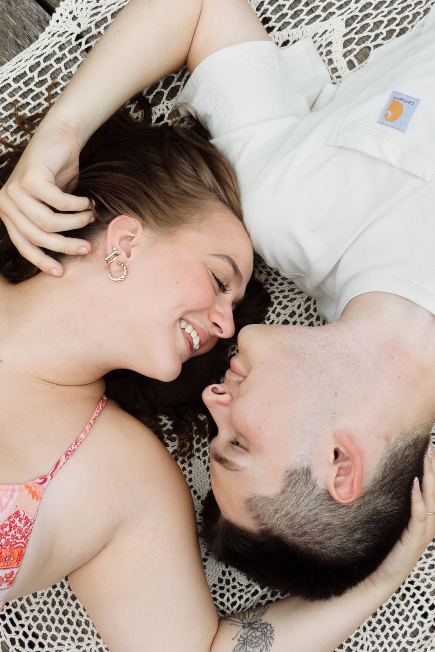 Happy couple lying together laughing and smiling face to face in a warm romantic portrait.