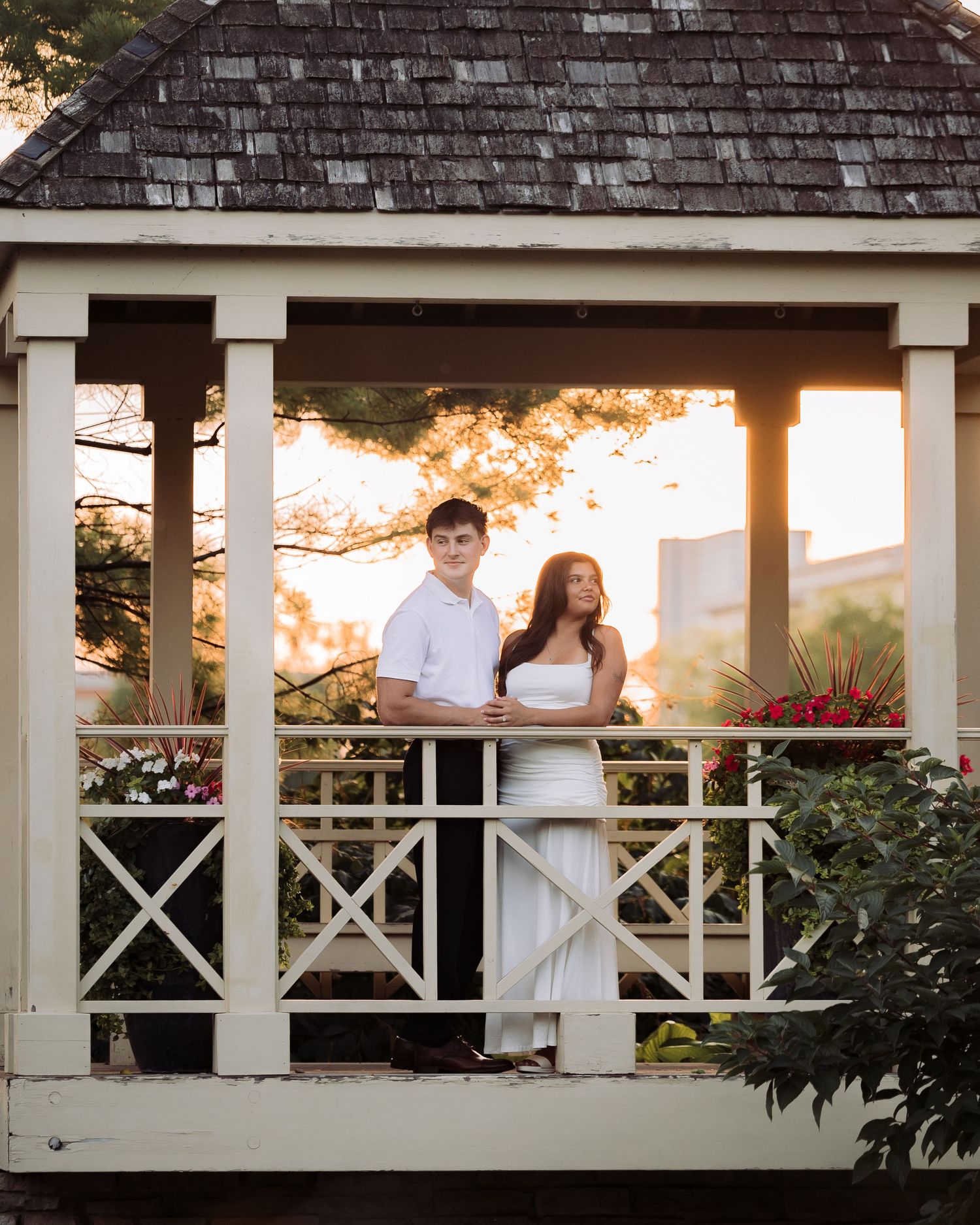 Couple in white outfits standing together in a charming gazebo at golden hour sunset.