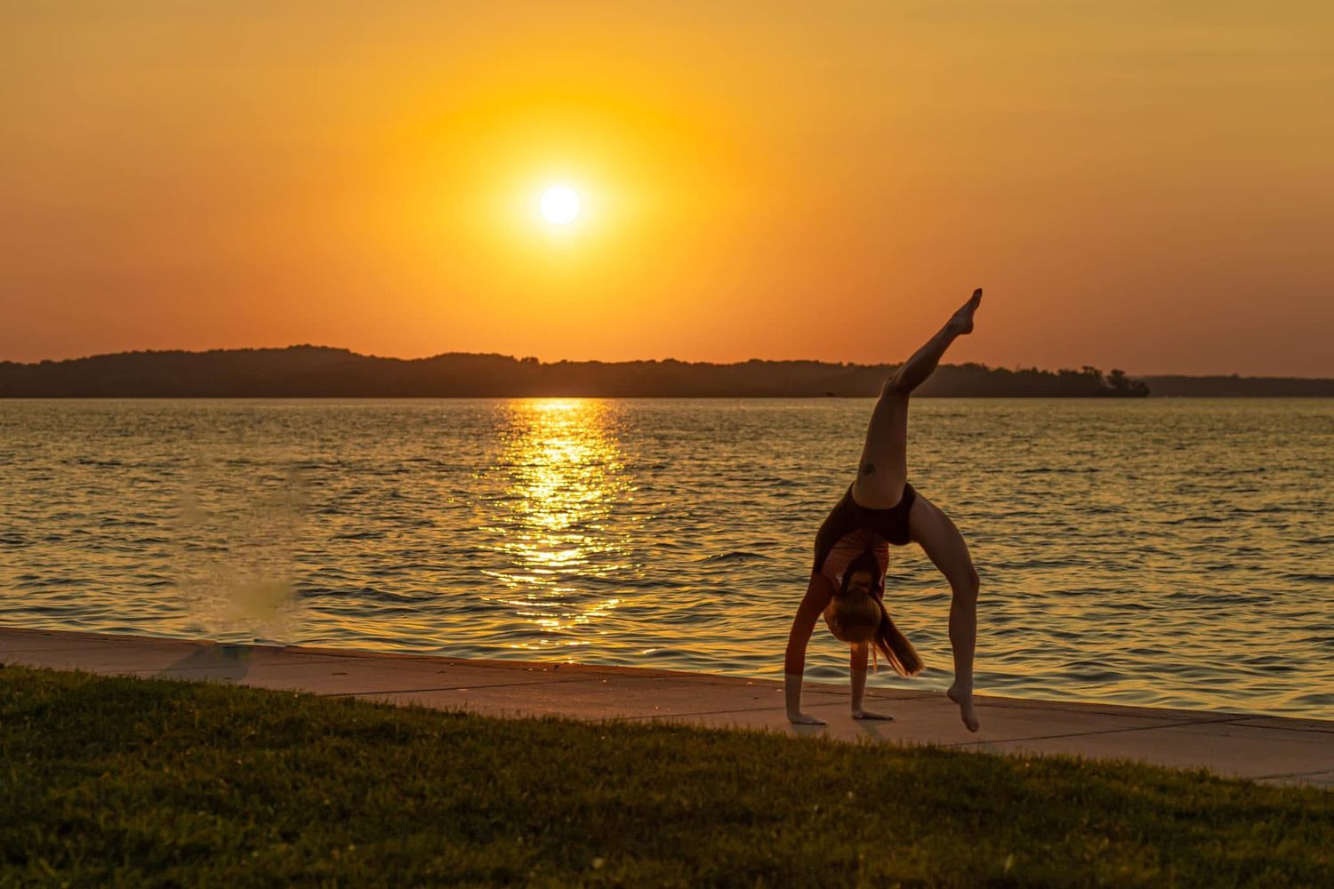 A silhouette of a person doing a cartwheel on a lakeside beach during a stunning golden sunset.