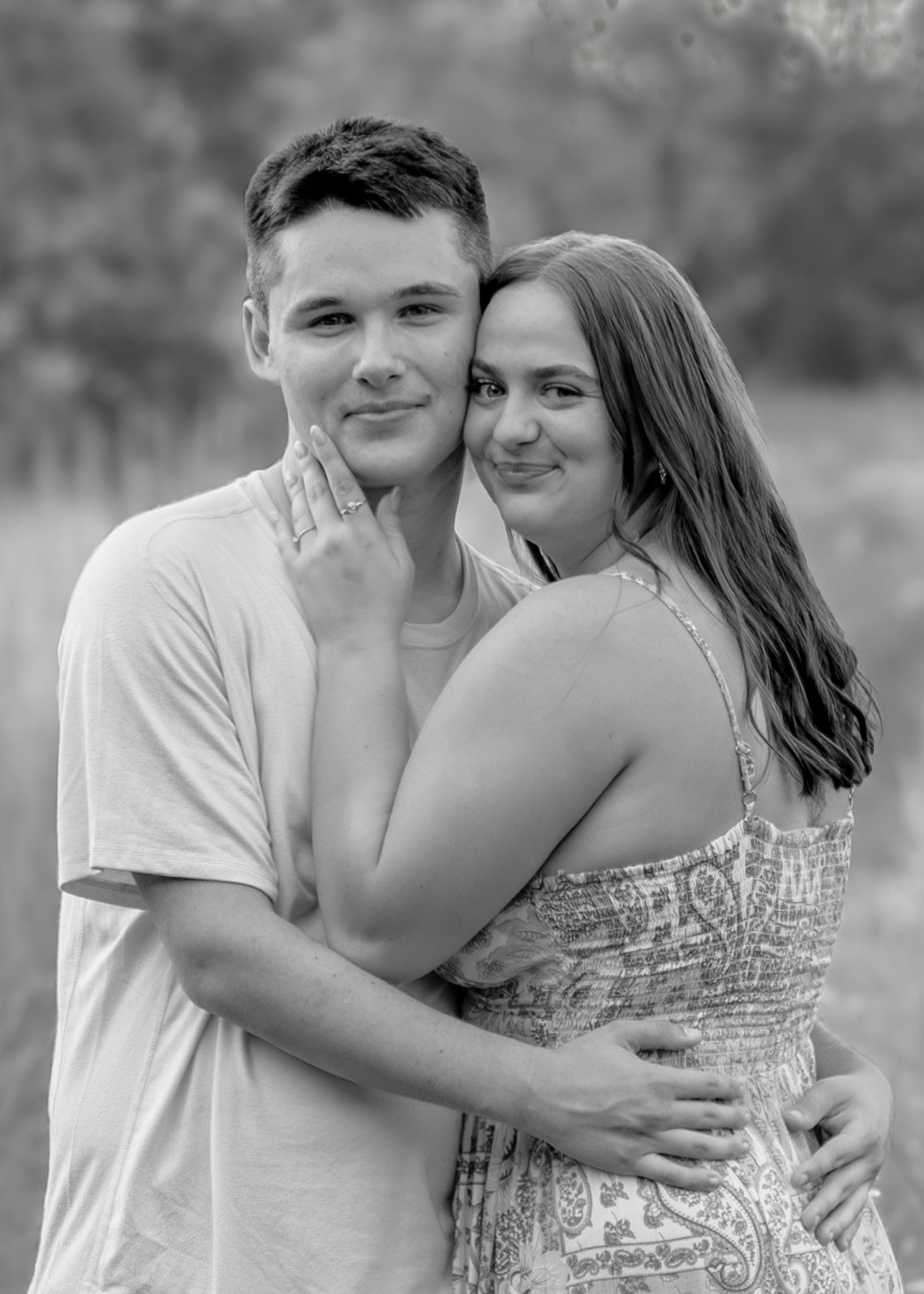 Black and white portrait of a young couple embracing and smiling in an outdoor setting.