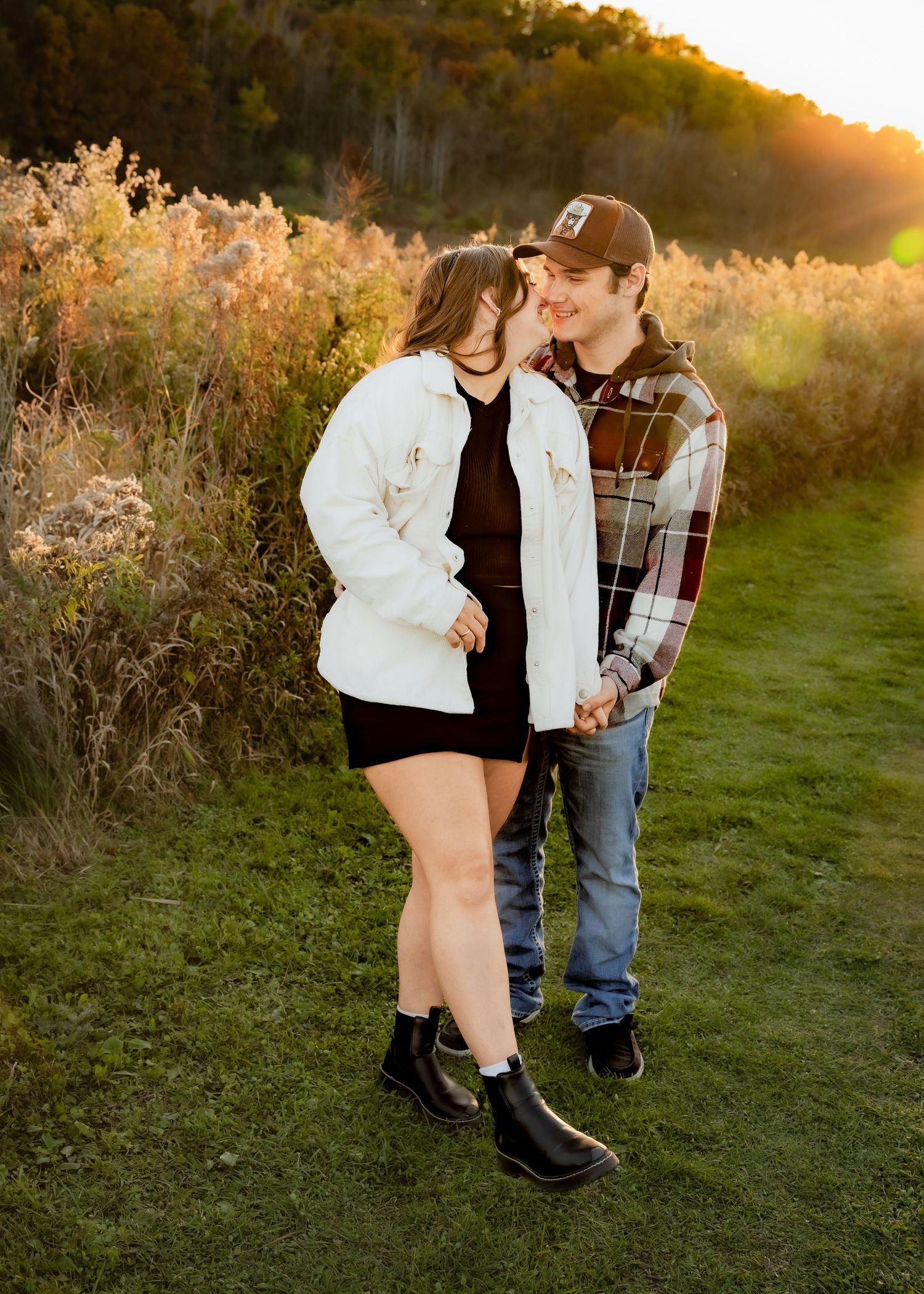Couple sharing a romantic moment on grassy path surrounded by golden sunset meadow.
