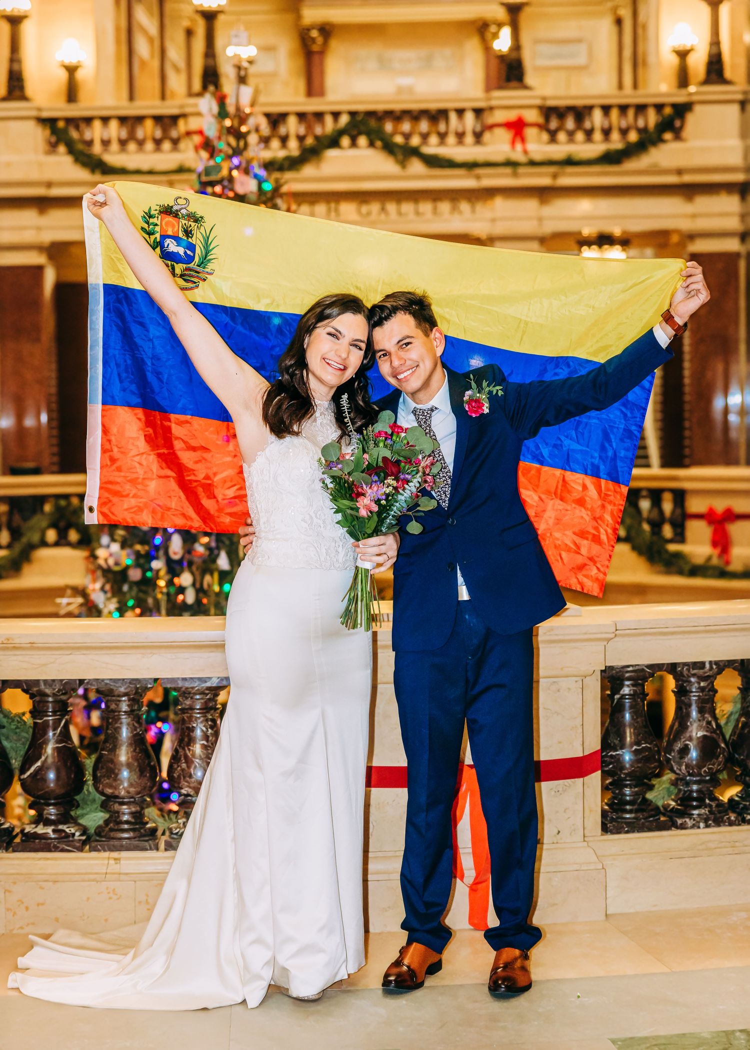 Joyful newlyweds hold Venezuelan flag high in colorful photo inside decorated capitol building.