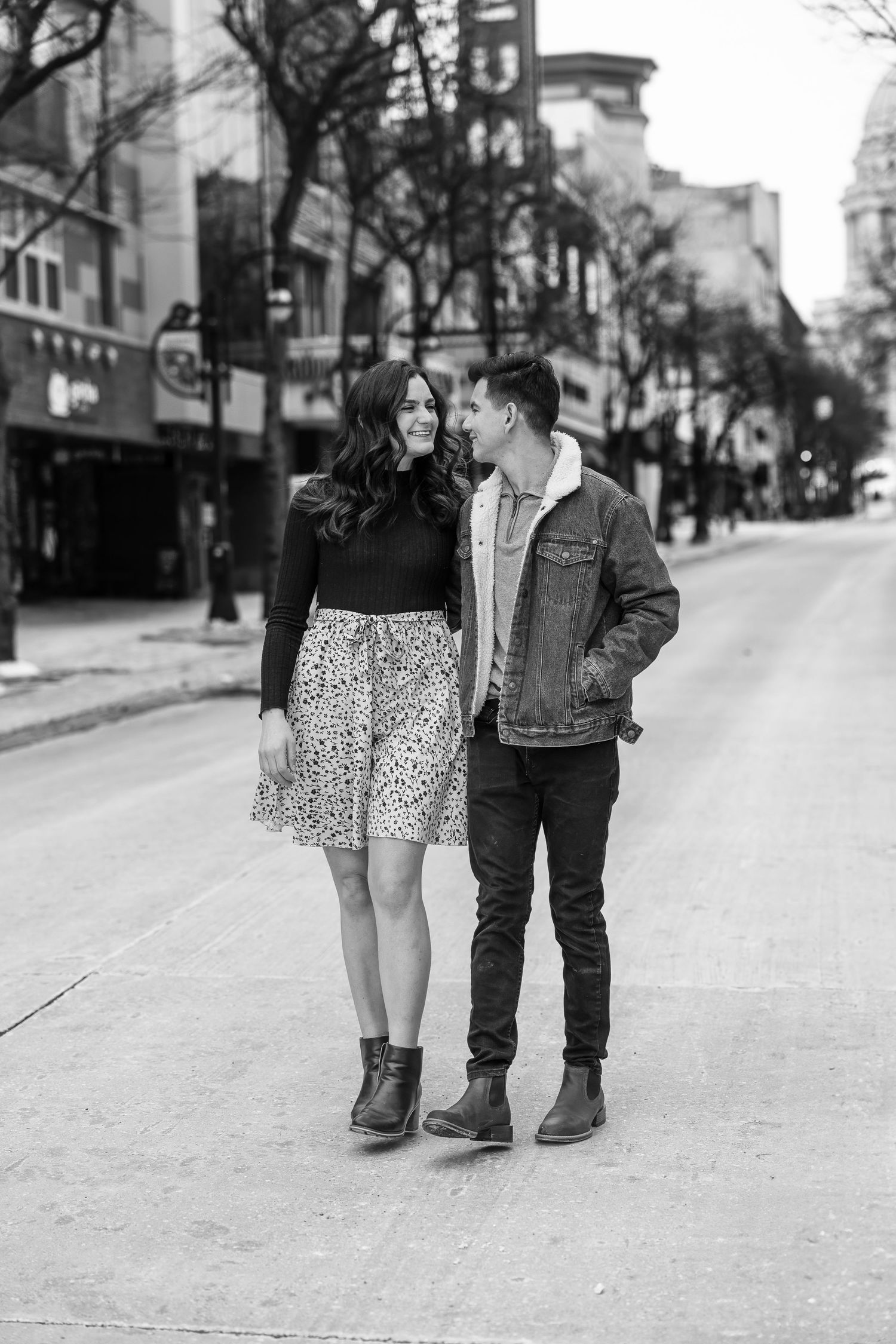 Black and white photo of a couple smiling at each other on an urban street.
