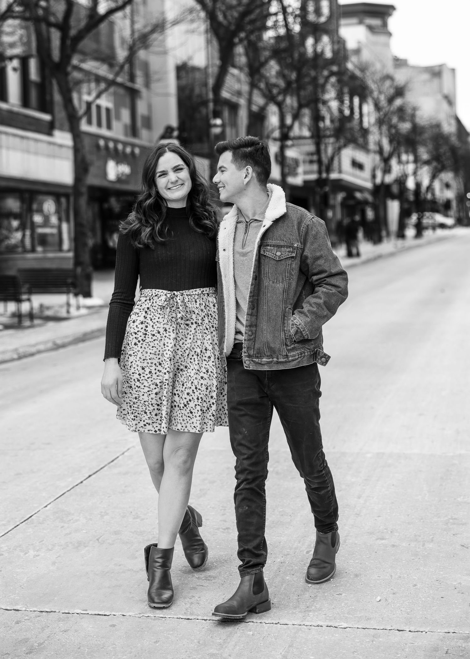Black and white photo of couple walking and smiling on an urban street, woman in floral skirt.