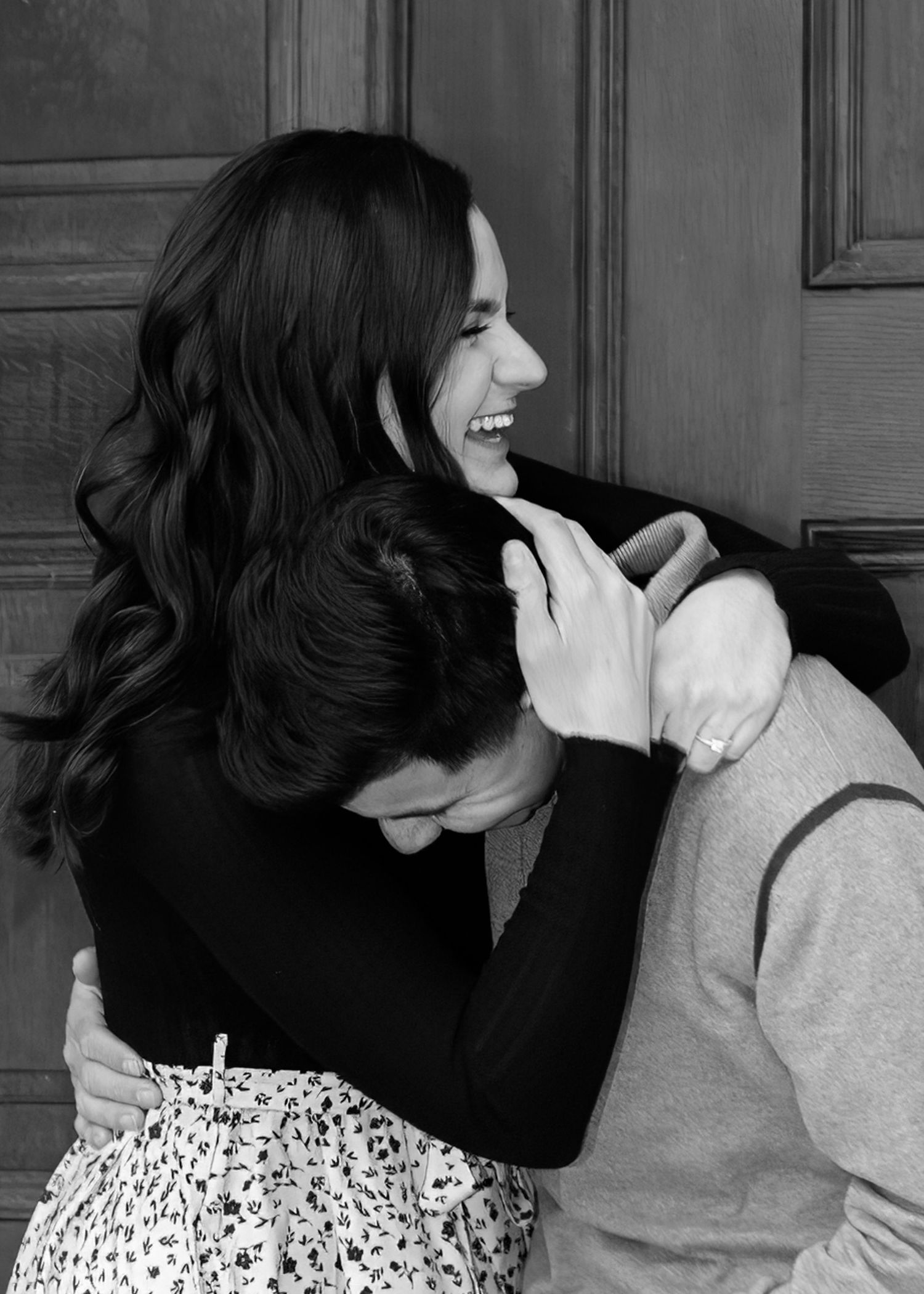 Black and white photo of a woman laughing joyfully while embracing her partner against a wooden door.