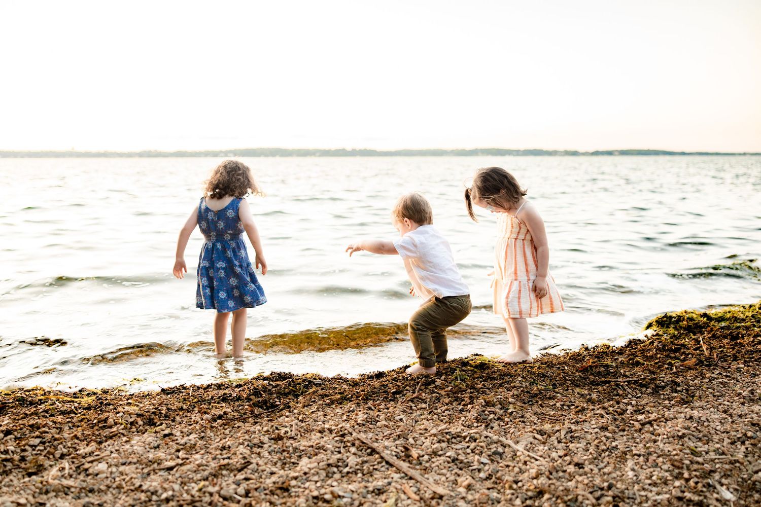 Three children playing on a rocky beach shore near the ocean waves on a sunny day.