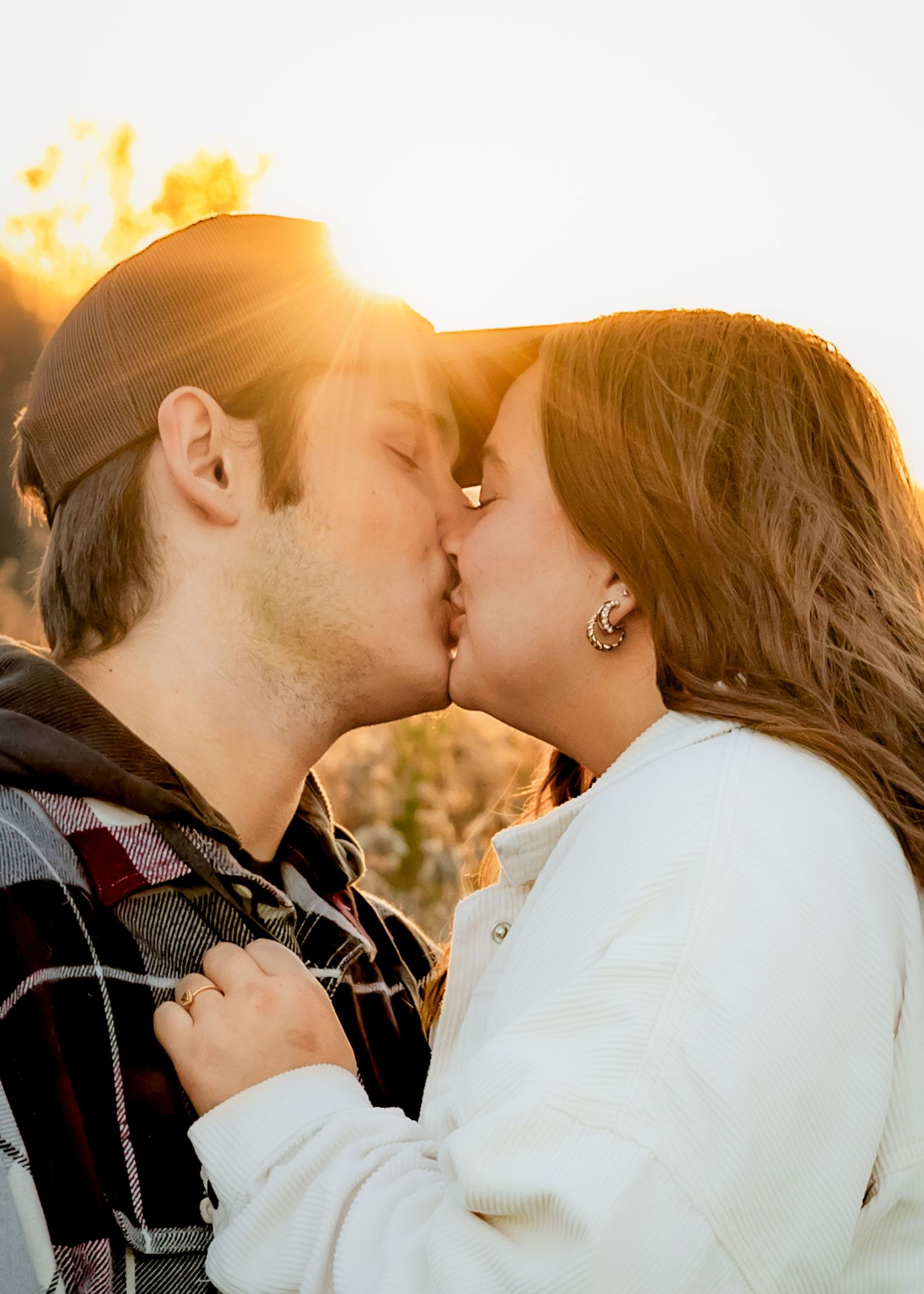 Couple sharing a romantic kiss at golden hour with warm sunlight glowing behind them.