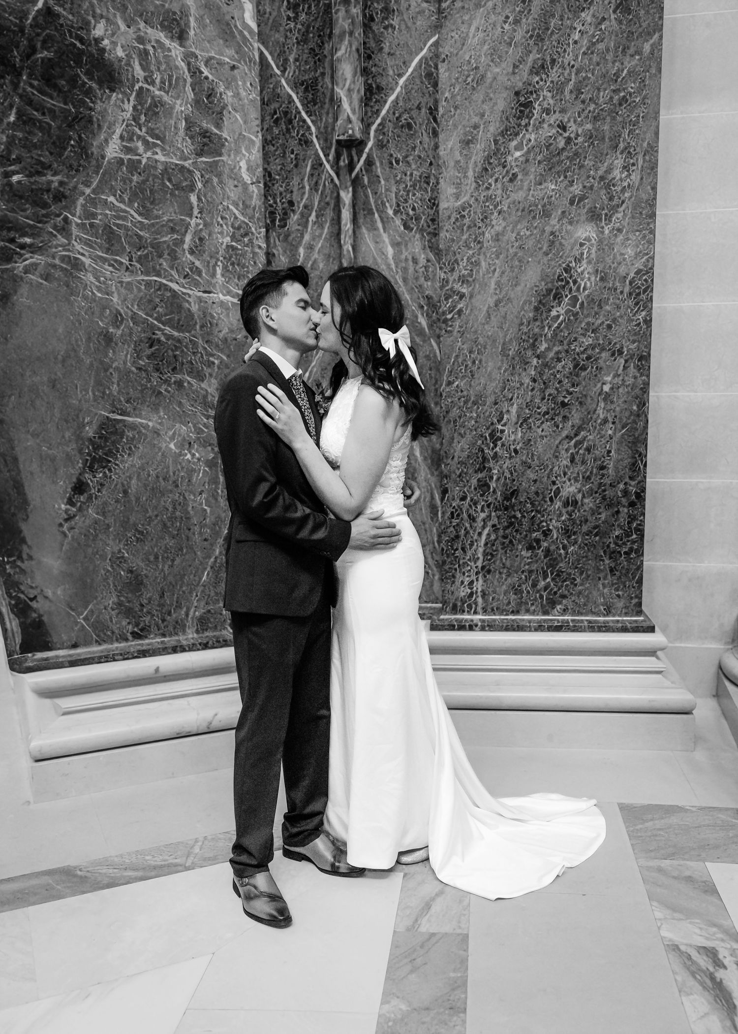 Elegant black and white wedding portrait of couple kissing before grand marble column backdrop.