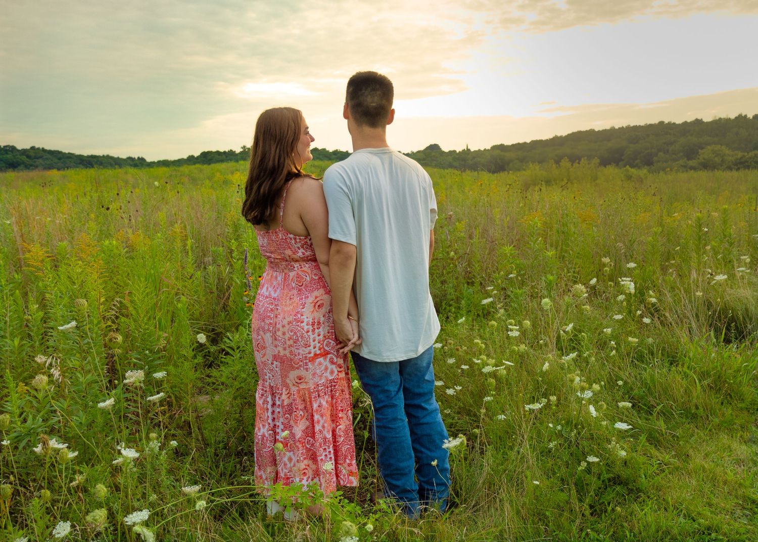 A couple standing hand in hand gazing at a stunning sunset over a lush green meadow.
