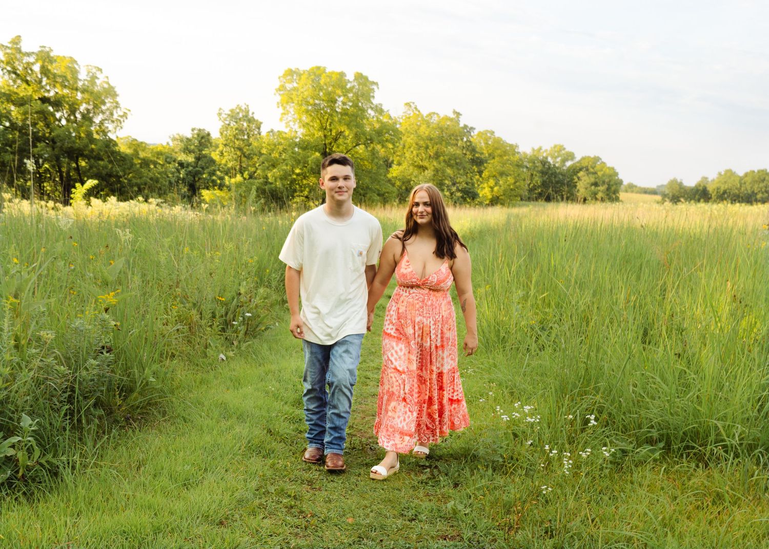 Happy couple holding hands walking along a lush green meadow path in summer.