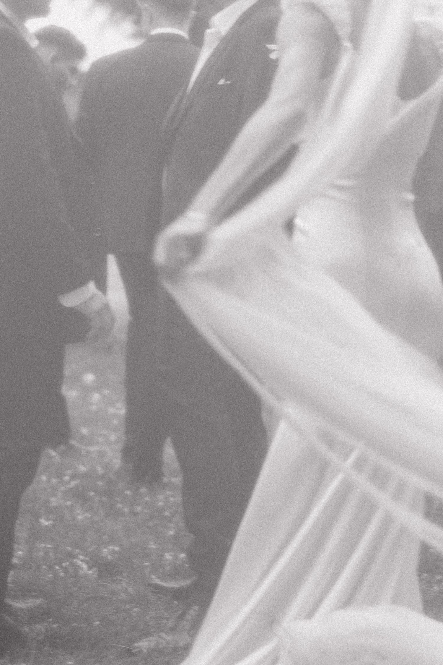 Black and white image showing close-up details of formal wedding attire with flowing white fabric against dark suits.