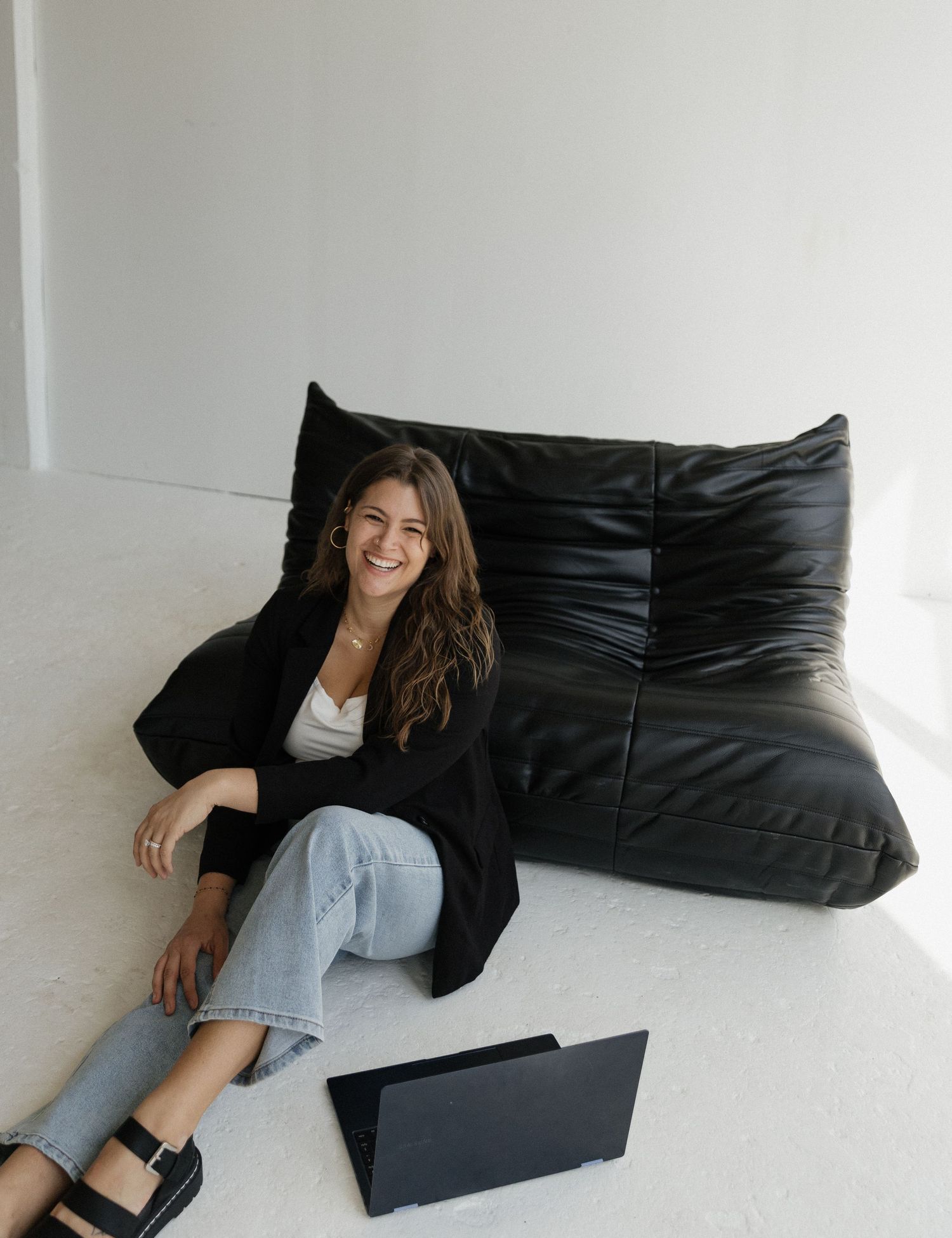 Woman in business casual attire working with laptop on modern black leather sofa.