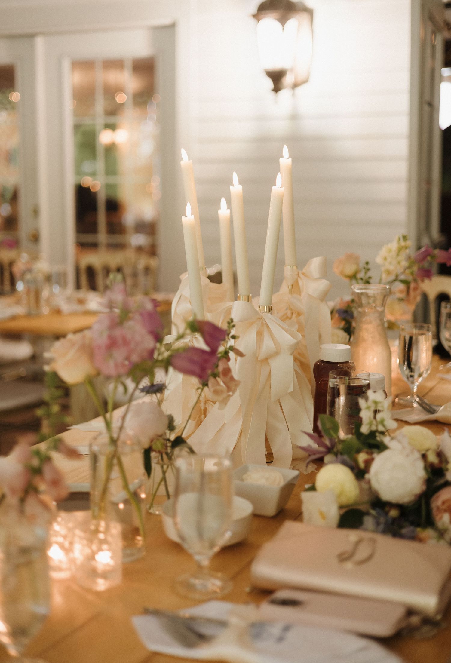 Elegant wedding table setting with white taper candles, soft pink flowers, and glowing votives creating romantic ambiance. maison albion