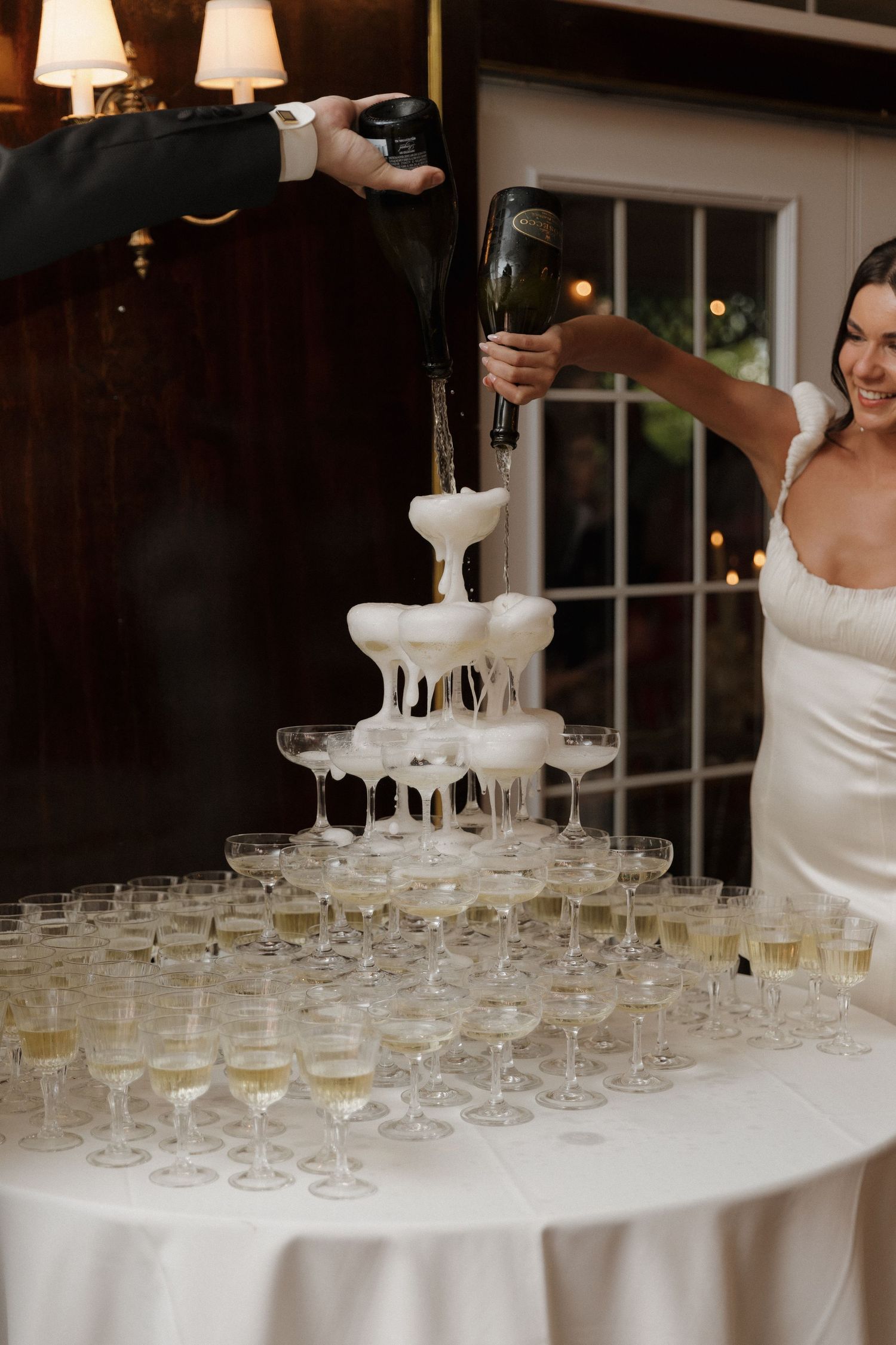 Champagne being poured into a tower of coupe glasses at an elegant wedding reception.