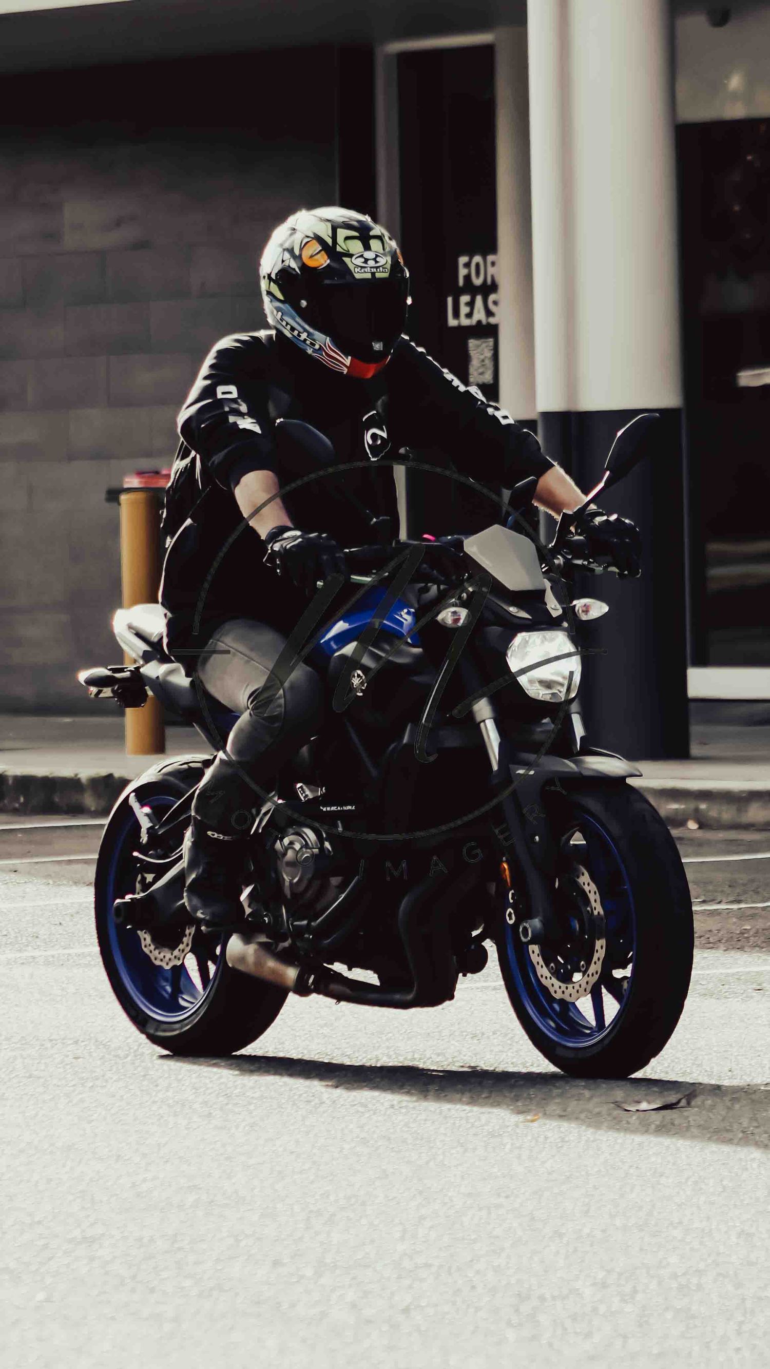 Motorcyclist in black gear and helmet riding a blue Yamaha MT sport bike on an urban street.